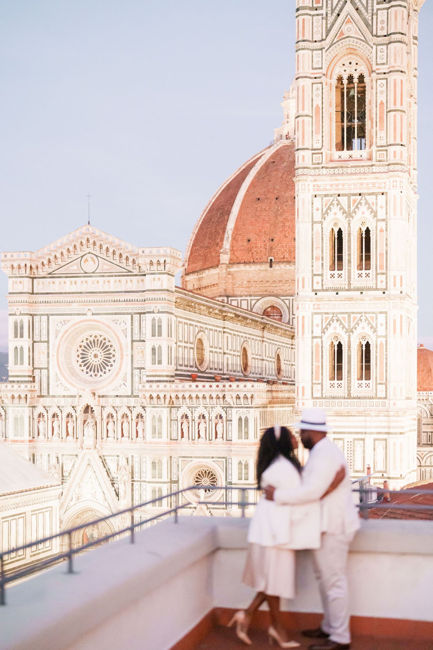 Romantic couple in white embracing on a rooftop terrace with Florence Cathedral dome and bell tower backdrop.