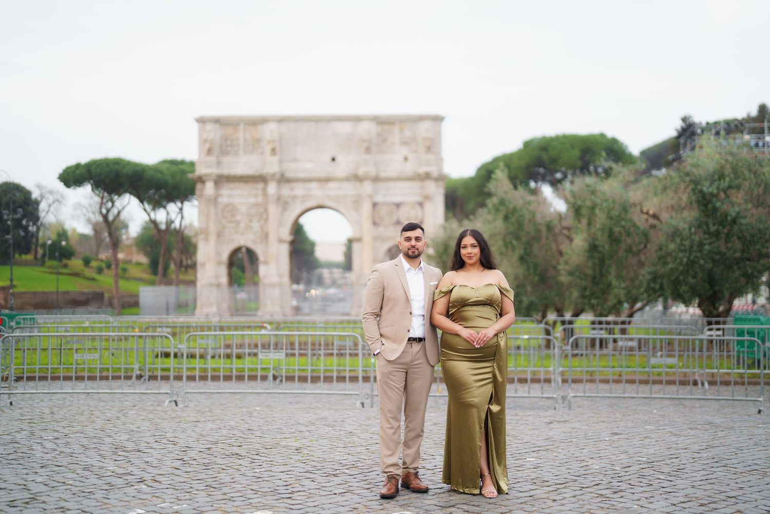 Couple in elegant attire posing before the Arch of Constantine in Rome during a maternity photoshoot.