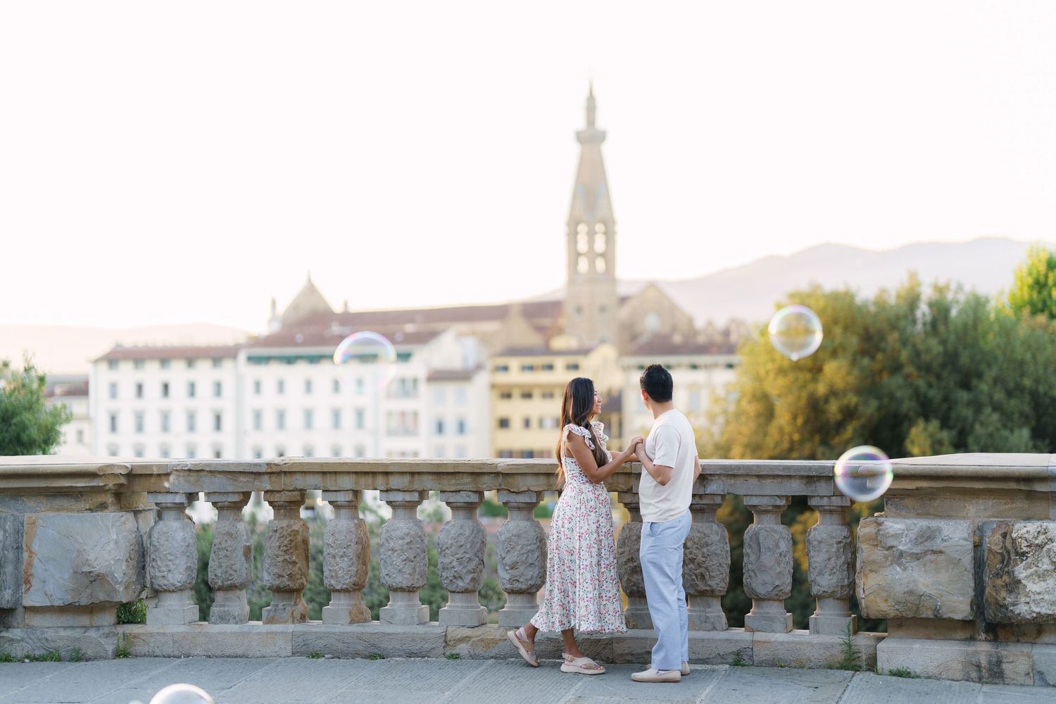 Couple walking on a scenic Florence terrace with soap bubbles, historic buildings and church tower in the golden hour background.