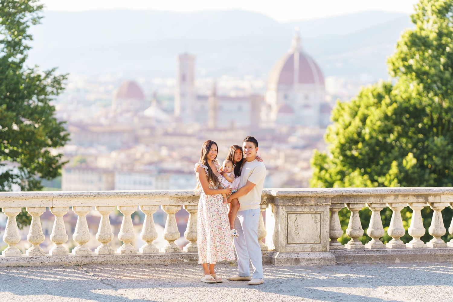 A couple embraces with a child on a sunlit terrace overlooking Florence's iconic Duomo cathedral in Italy.