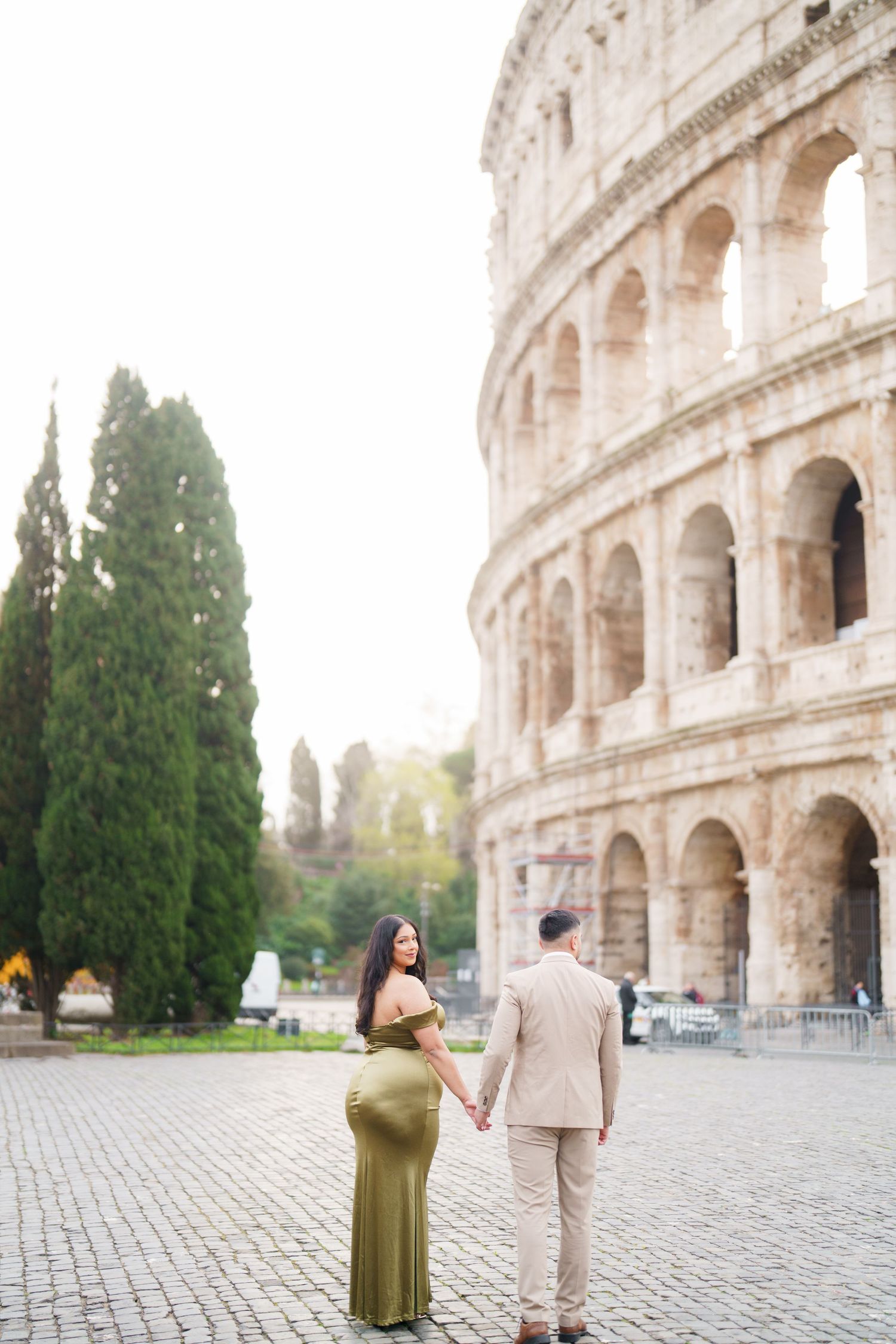 Couple holding hands in front of the Colosseum in Rome, woman in green gown, man in beige suit.