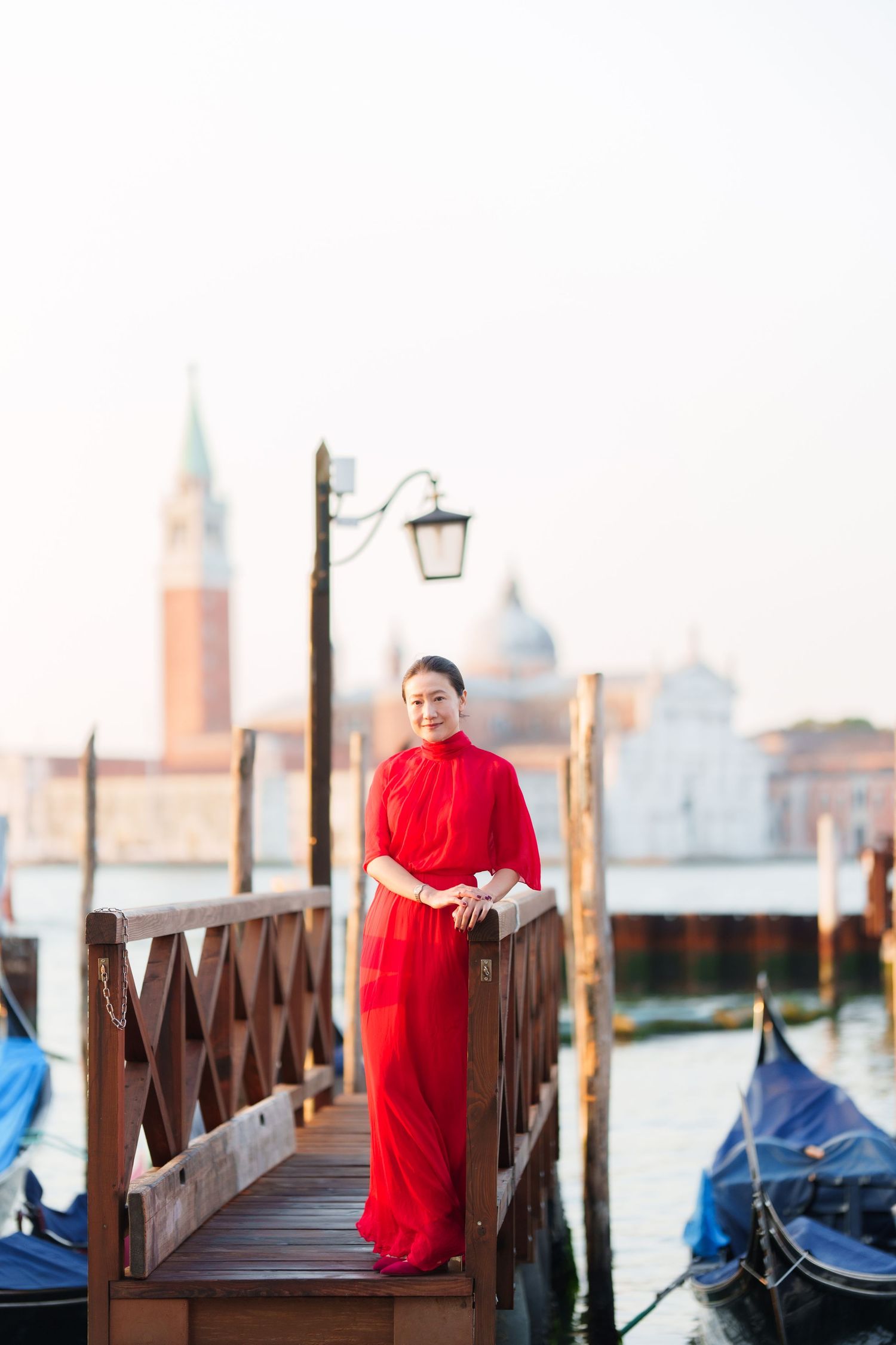 Woman in red dress posing on Venice gondola dock with San Giorgio Maggiore church in background.