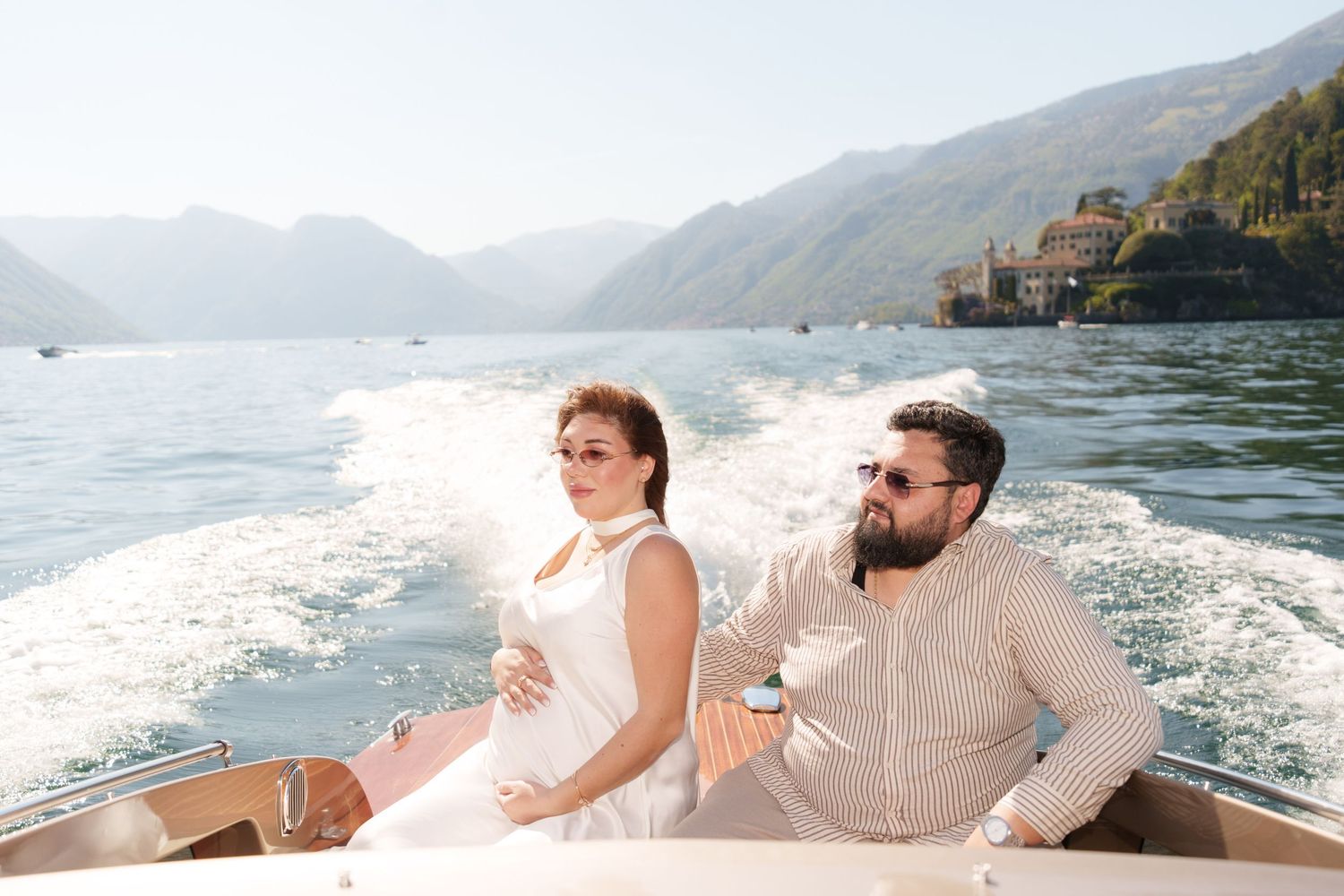 Couple sitting on a speedboat on Lake Como, Italy, with mountains and villas in the background.