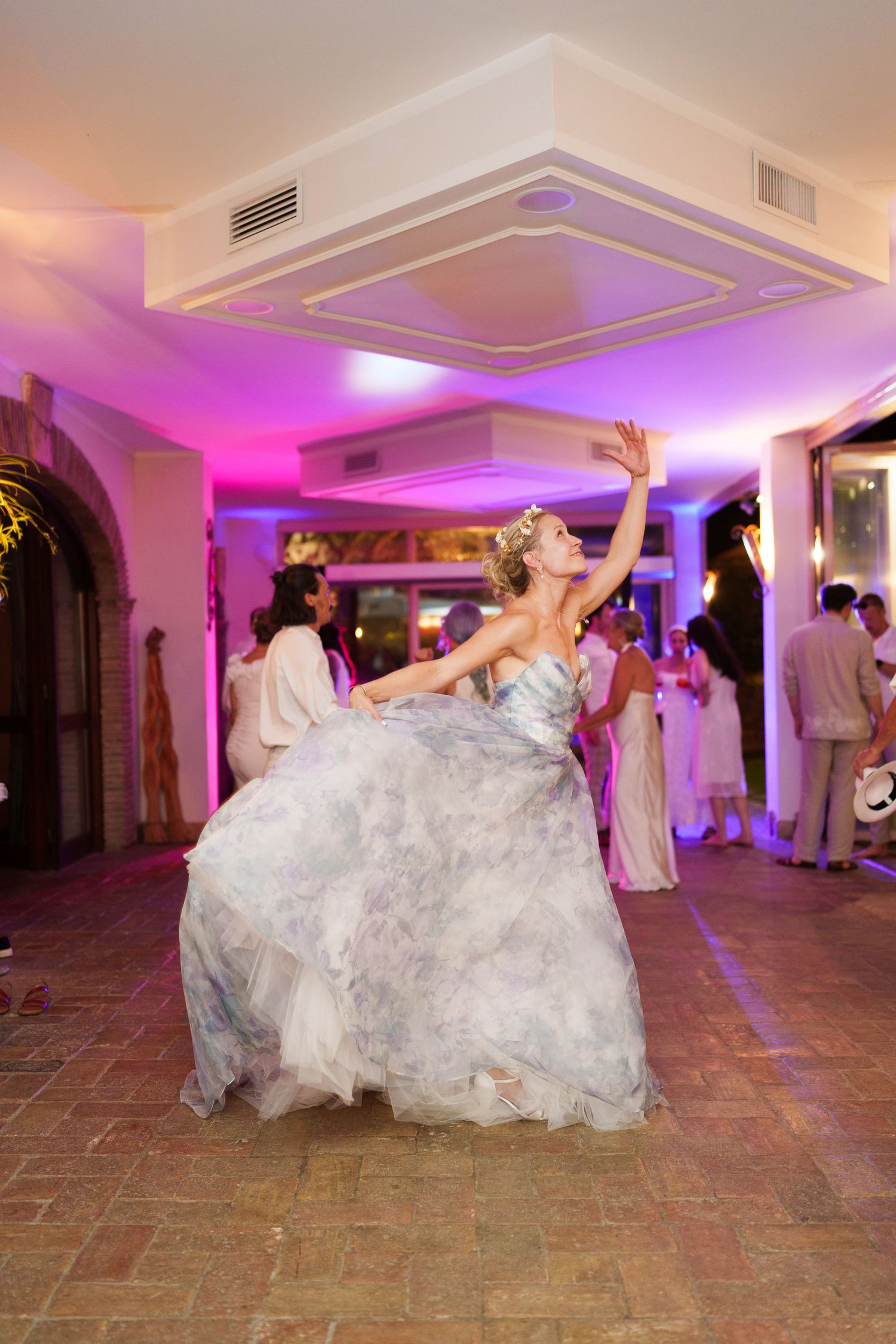 Bride in a flowing gray ball gown dancing joyfully at a wedding reception with colorful purple lighting.