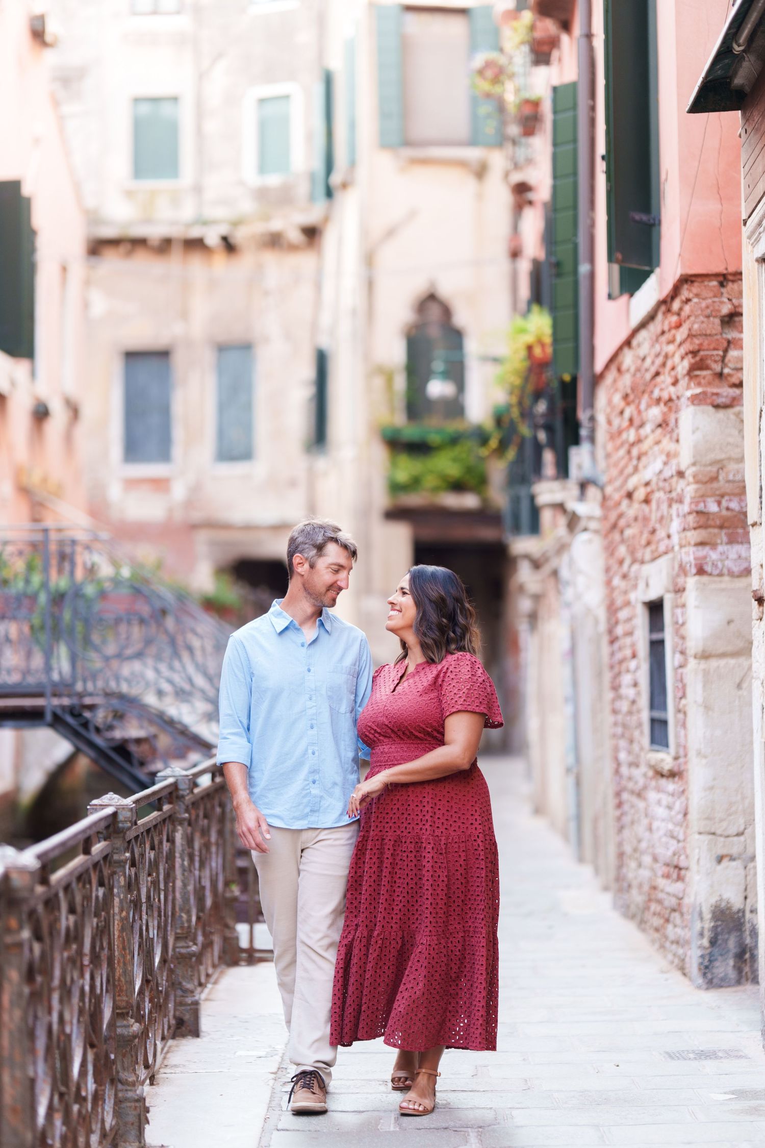 Couple walking hand-in-hand through a charming Venice alleyway, surrounded by historic brick buildings and a canal bridge.