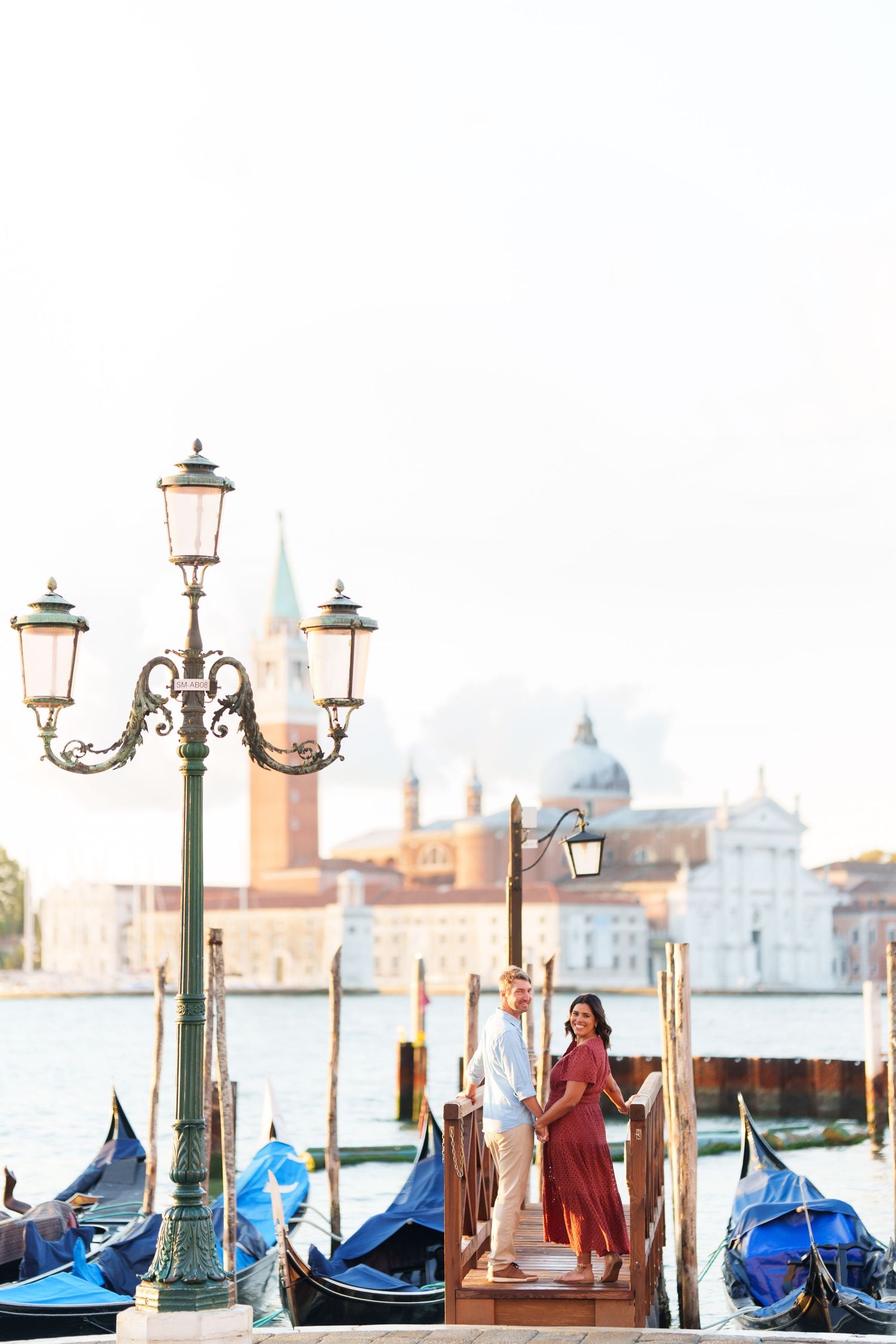 Romantic couple standing on a gondola dock in Venice, Italy, with San Giorgio Maggiore church in the background.