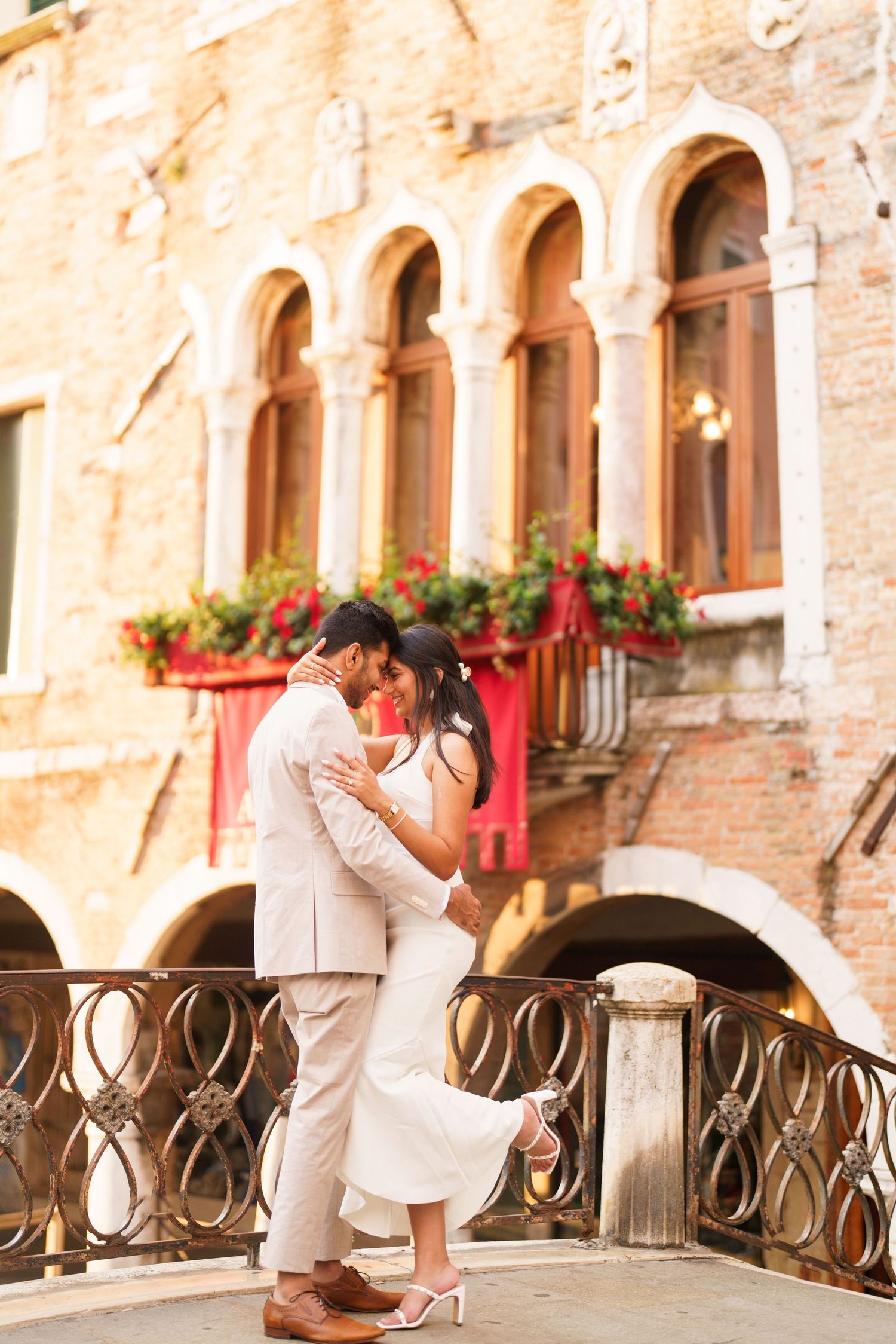 Couple in white outfits dancing romantically on a rustic Italian balcony with stone walls and flower boxes.