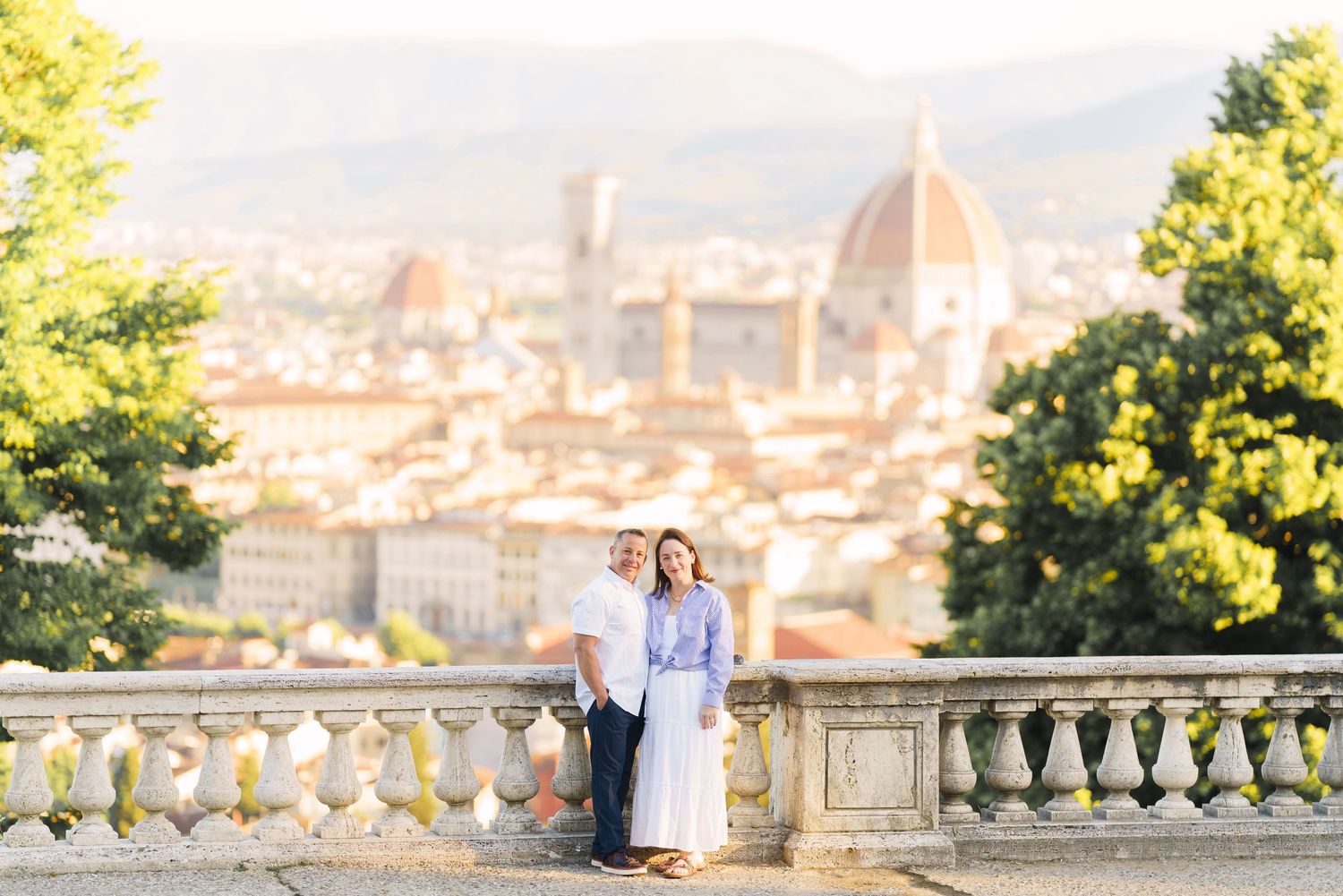 Couple poses on scenic overlook with panoramic view of Florence, Italy during destination wedding shoot.