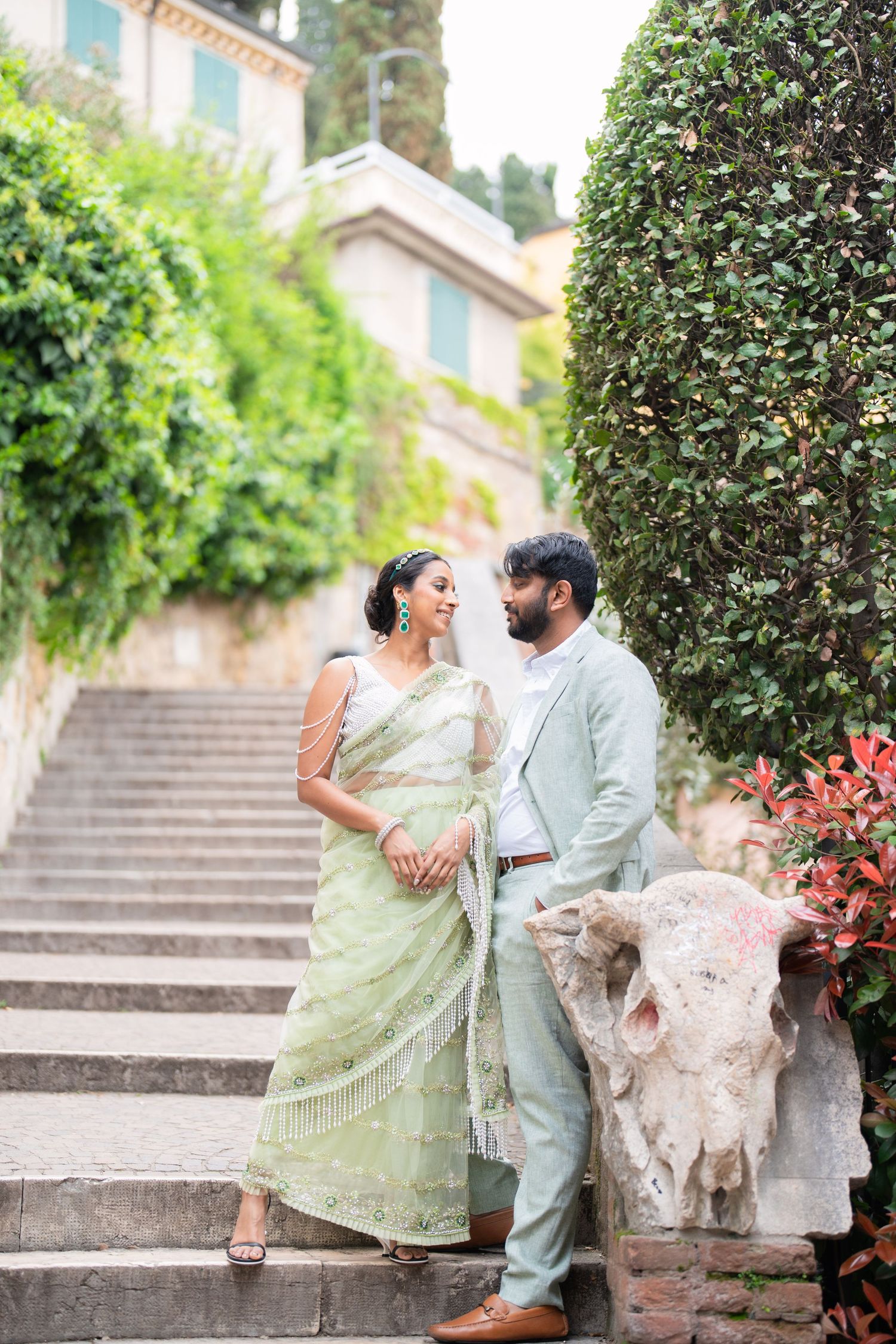 A couple in traditional Indian attire share romantic moments on stone steps surrounded by greenery.