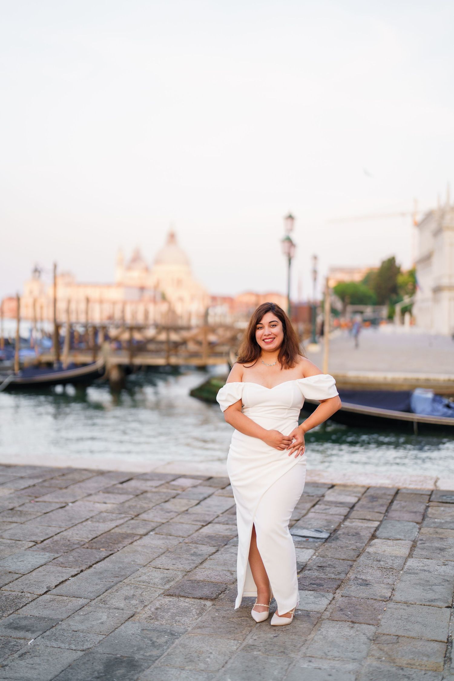 A person in a white dress sits gracefully on stone steps near a waterfront in Venice, Italy.