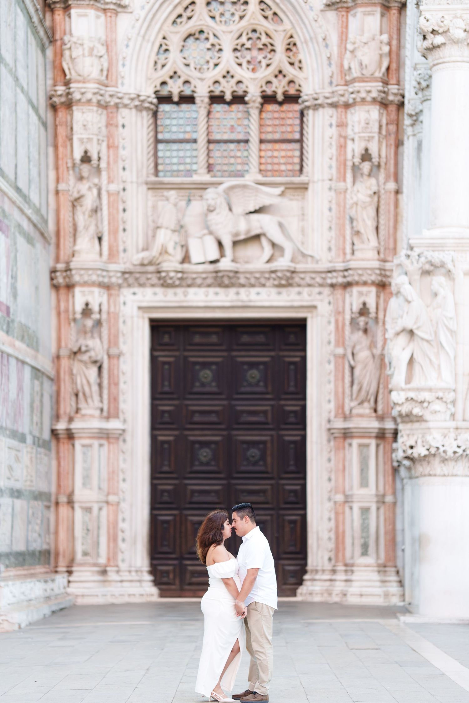 photographer venA couple shares romantic moments in front of an ornate Gothic cathedral with elaborate stone carvings and dark wooden doors.