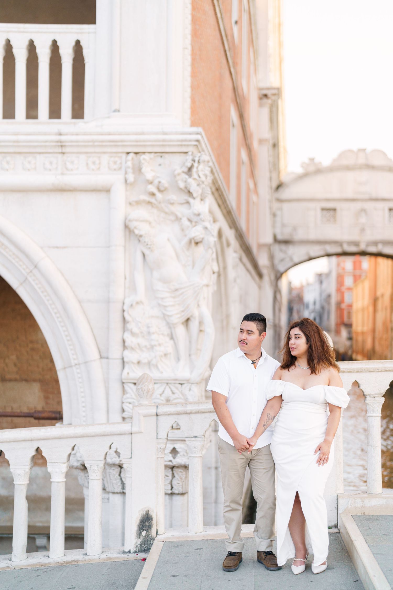 A couple poses together in front of ornate white marble columns and arches in Venice, Italy.