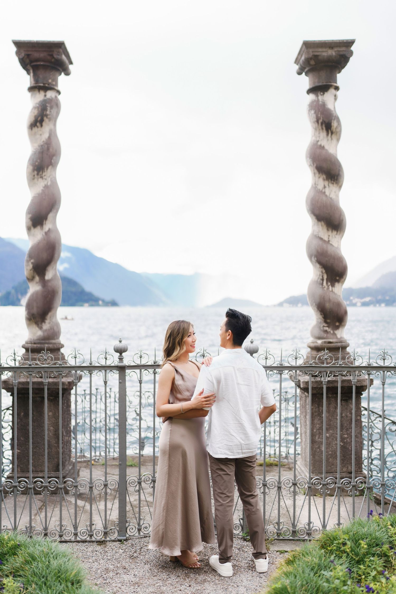 Couple enjoying a romantic moment on an elegant stone balcony overlooking Lake Como and mountains in Italy.