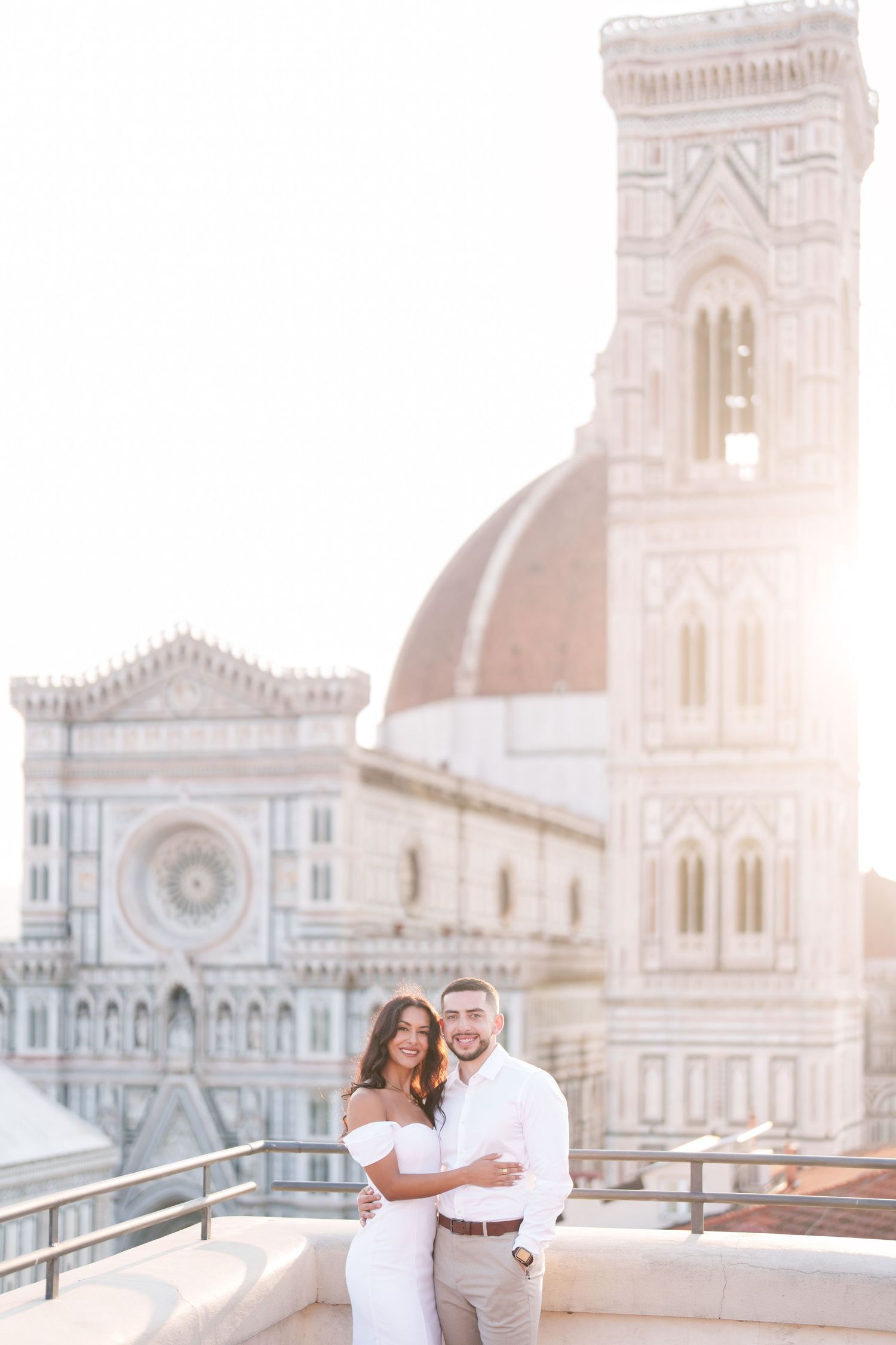 Couple poses on rooftop terrace with Florence Cathedral and Giotto's Bell Tower in background during sunset.