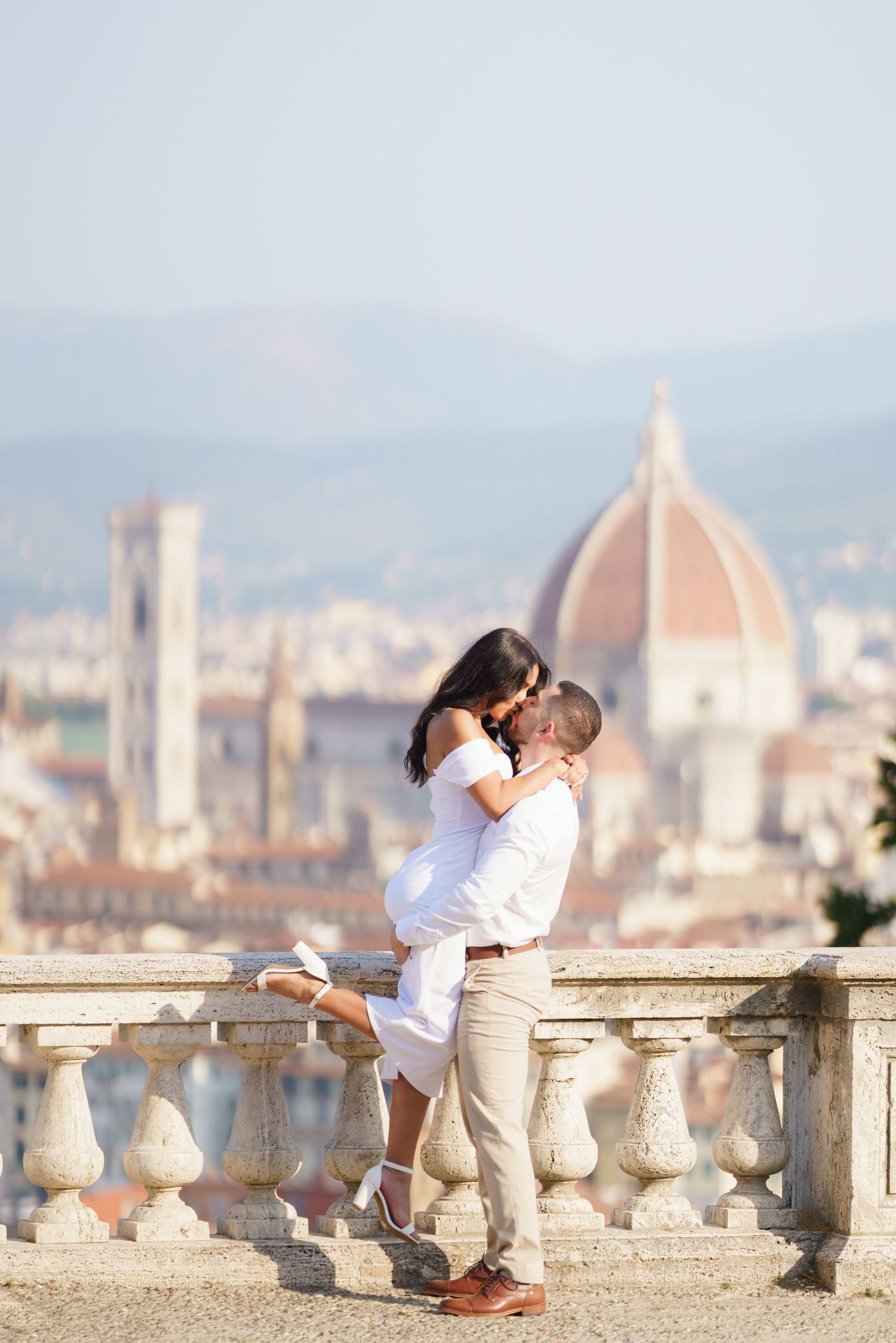 A romantic couple embraces at a scenic overlook with Florence's Duomo cathedral and cityscape in the background.