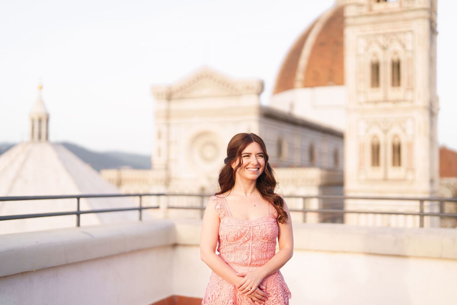 A person in a pink floral dress poses gracefully at a European architectural landmark during golden hour.