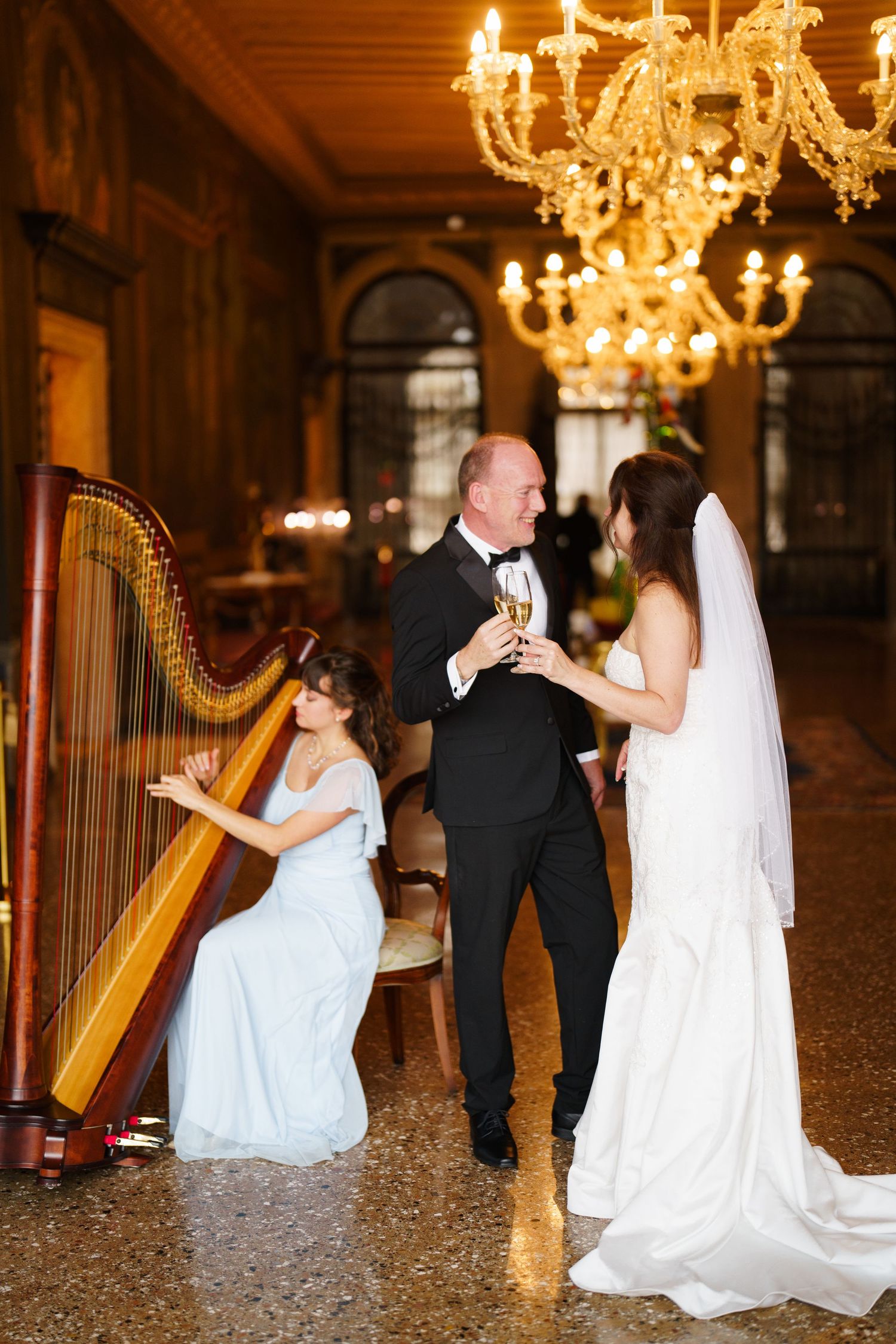 Elegant wedding couple dances in a grand ballroom under sparkling crystal chandeliers.
