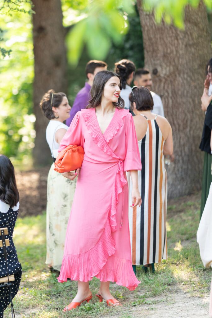 Wedding attendees in colorful dresses gather under trees at an outdoor celebration.