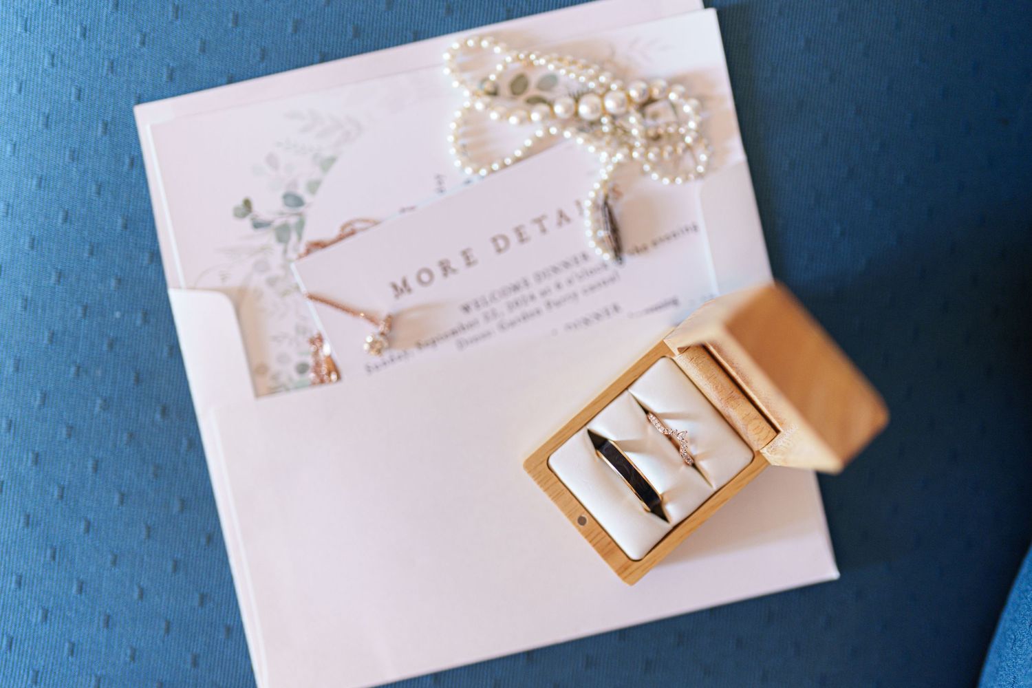 Wedding invitation and accessories including pearls and gold details on blue background.