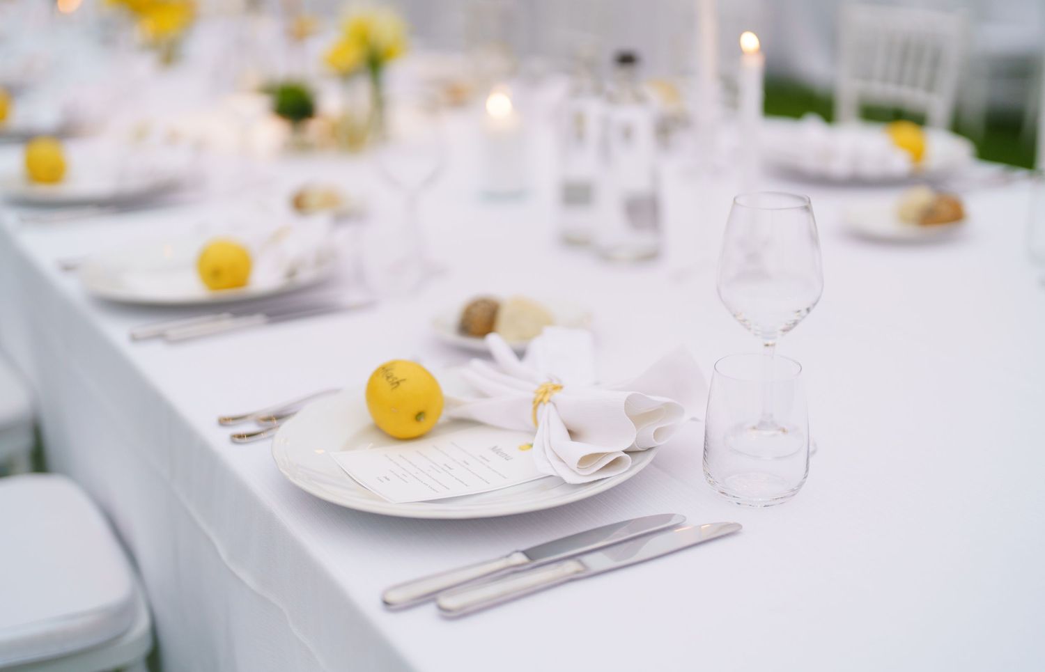 Elegant table setting with white plates, wine glasses and yellow floral accents.