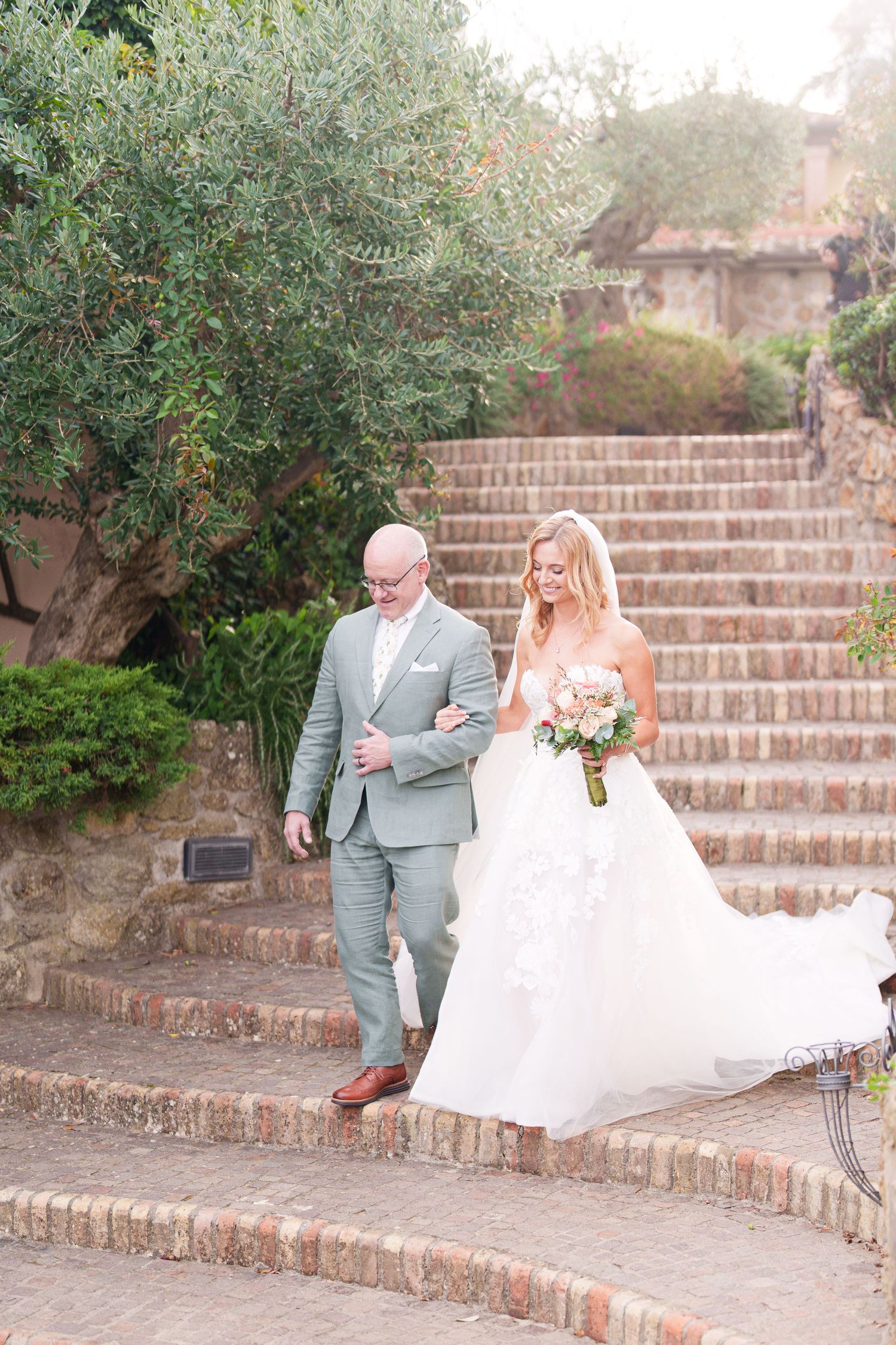 Couple walking and laughing together on brick stairs surrounded by greenery.