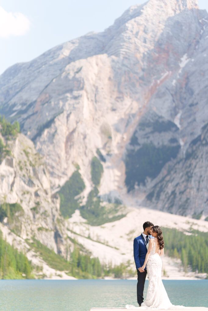 Elegant wedding photography by a turquoise alpine lake surrounded by towering mountain peaks.