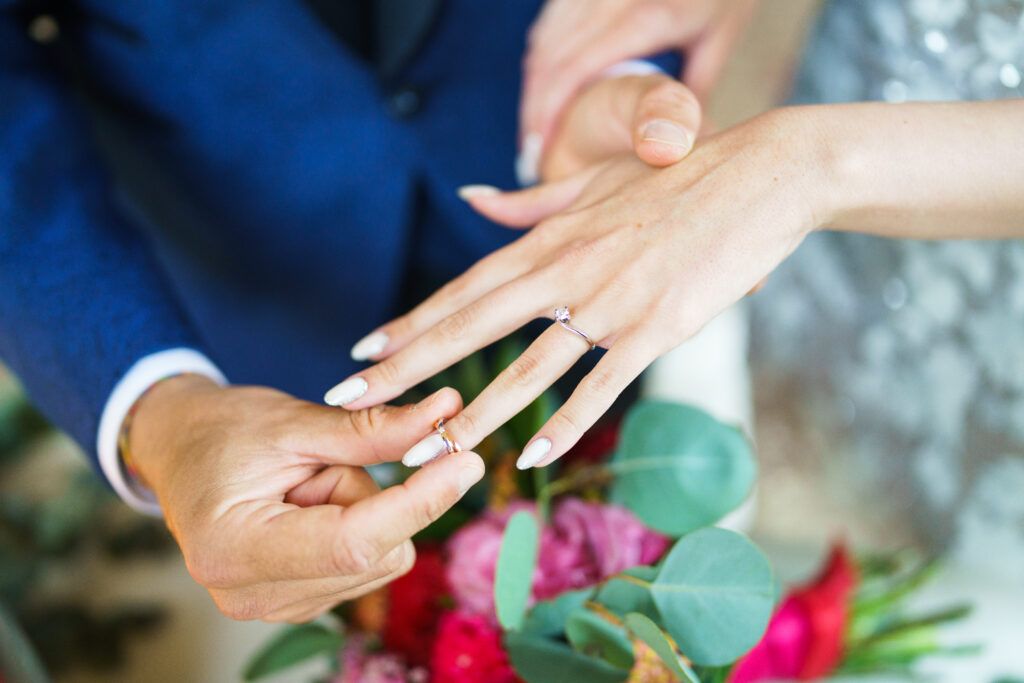 Close-up of hands during a wedding ceremony in an elegant indoor setting.
