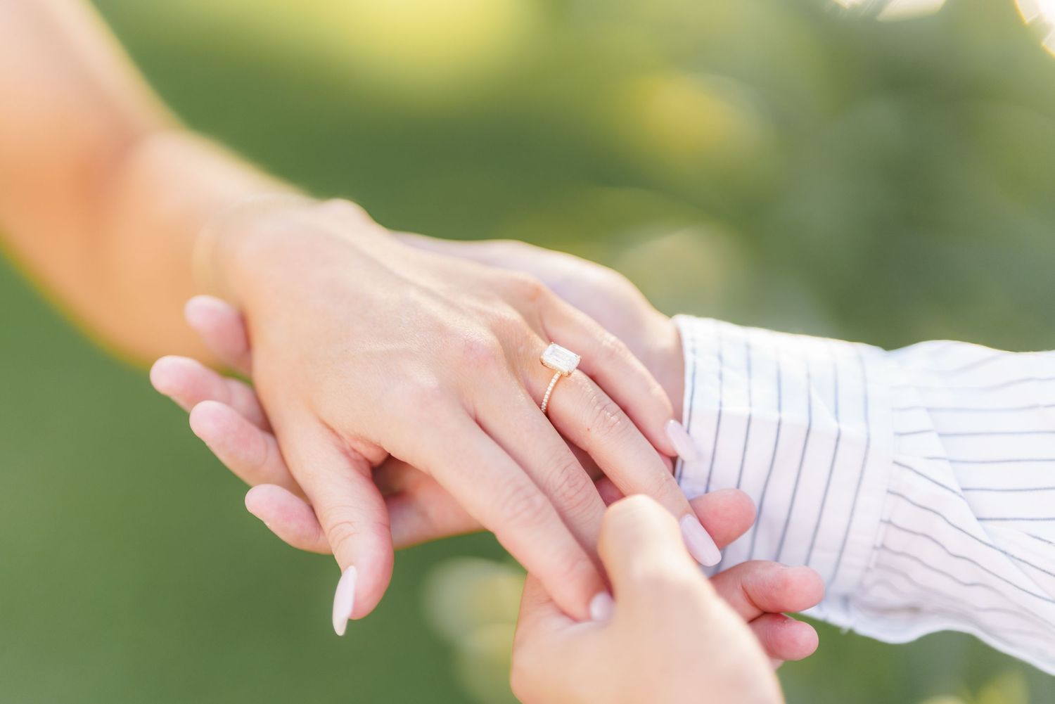 A close-up view of hands exchanging wedding rings during an outdoor ceremony in natural sunlight.