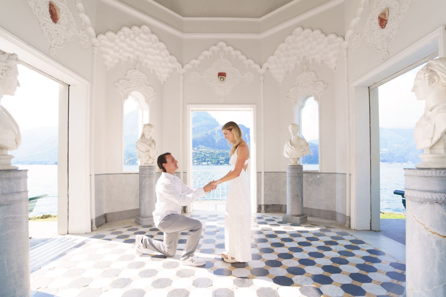 A white columned walkway with blue and white checkered floor tiles overlooking a scenic mountain landscape.