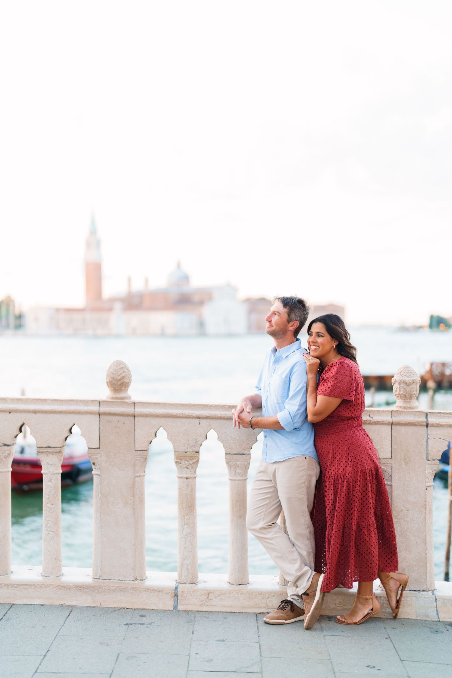 Couple embracing on a marble balustrade in Venice, Italy, with San Giorgio Maggiore island in the background.