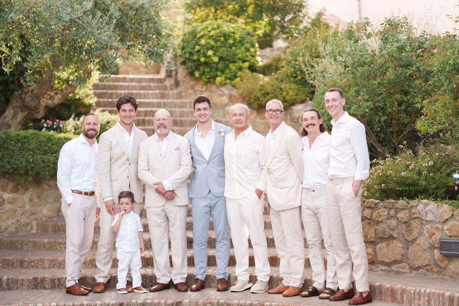 Groomsmen and groom posing together in neutral tones at an outdoor wedding venue with stone steps.