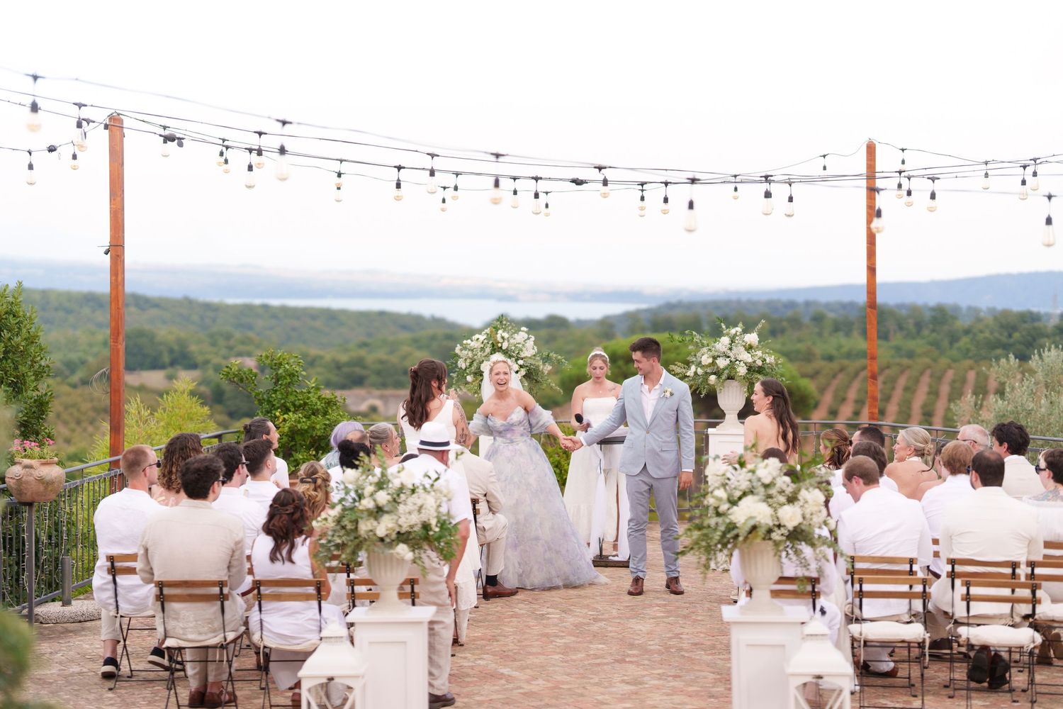 Outdoor vineyard wedding ceremony with string lights, floral arch, and scenic mountain views.
