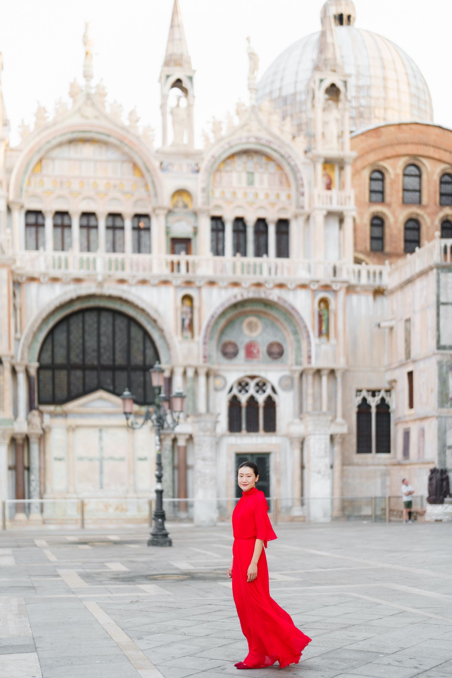 Woman in red dress posing in St. Mark's Square, Venice, with the ornate Basilica di San Marco facade behind her.
