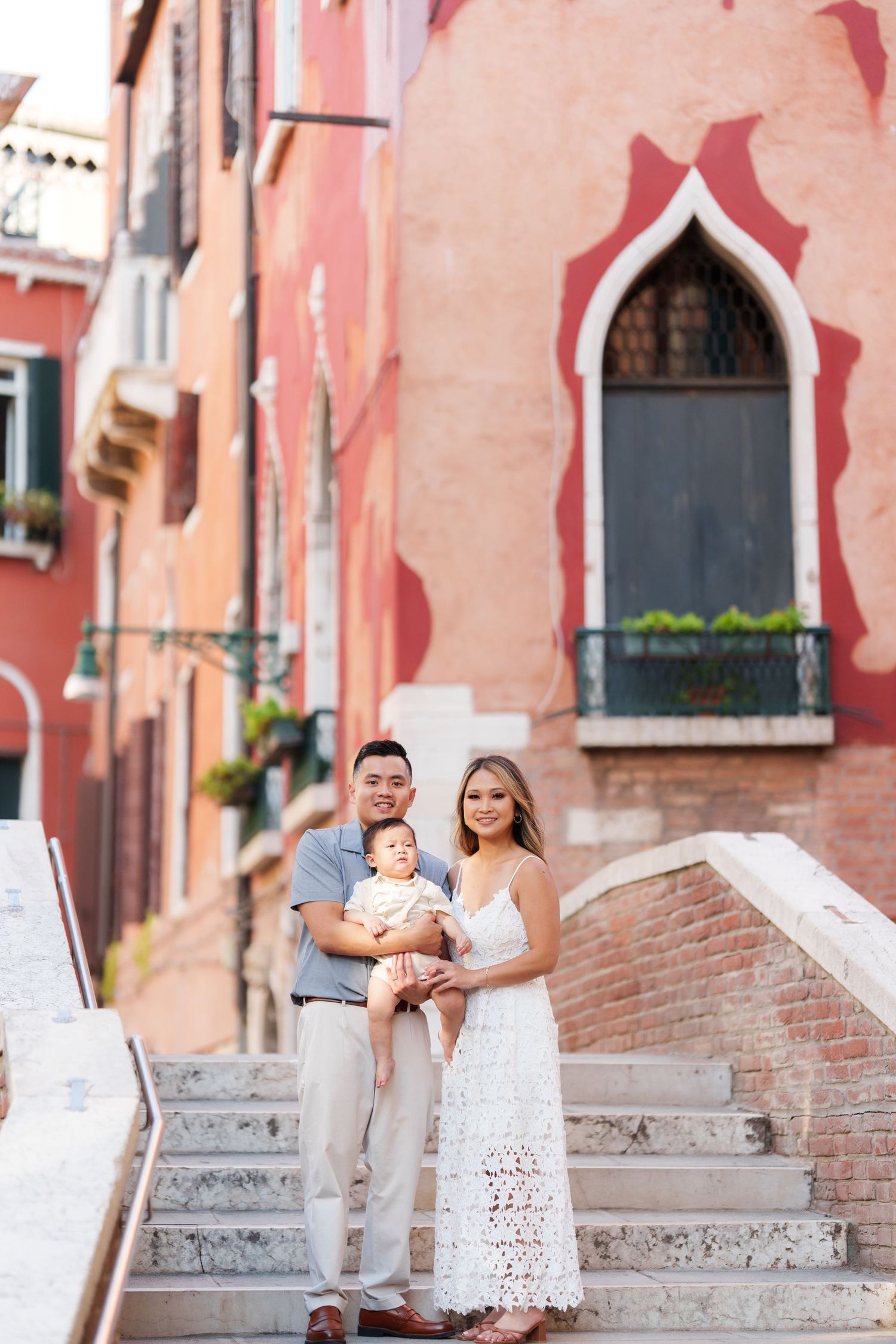 Family of three poses on Venice steps with colorful historic buildings backdrop.