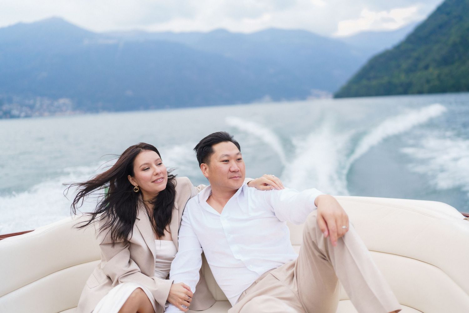 Couple enjoying a boat ride on a scenic mountain lake with wind blowing on a sunny day.