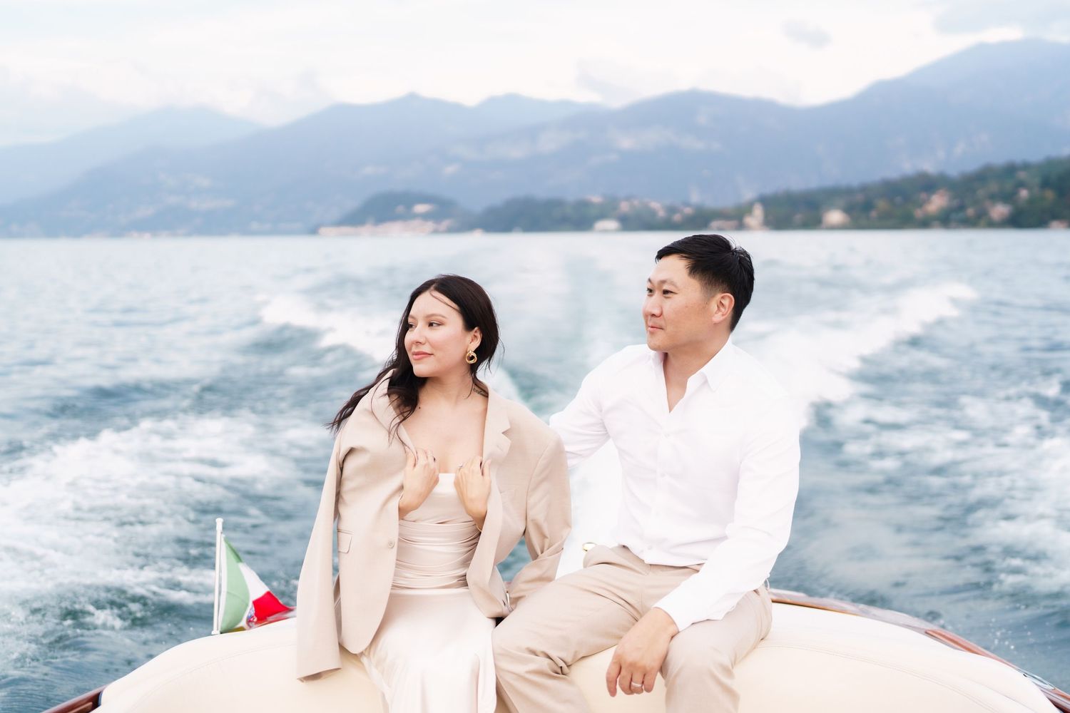 A couple sits together on a boat enjoying a romantic moment on the water with mountains in the background.
