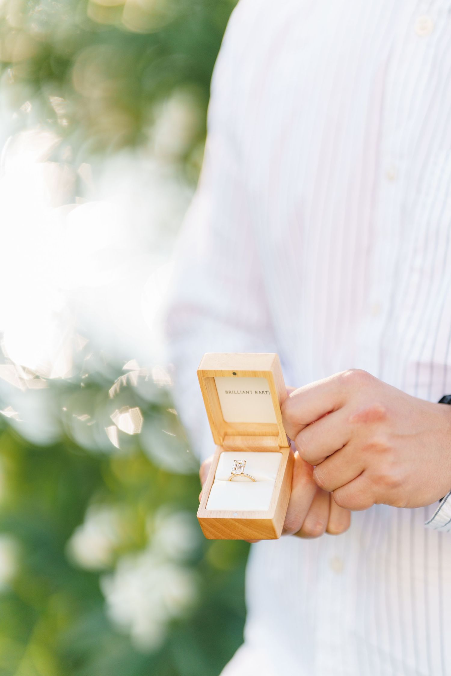 Close-up view of hands holding a small orange gift box against a soft white and green bokeh background.
