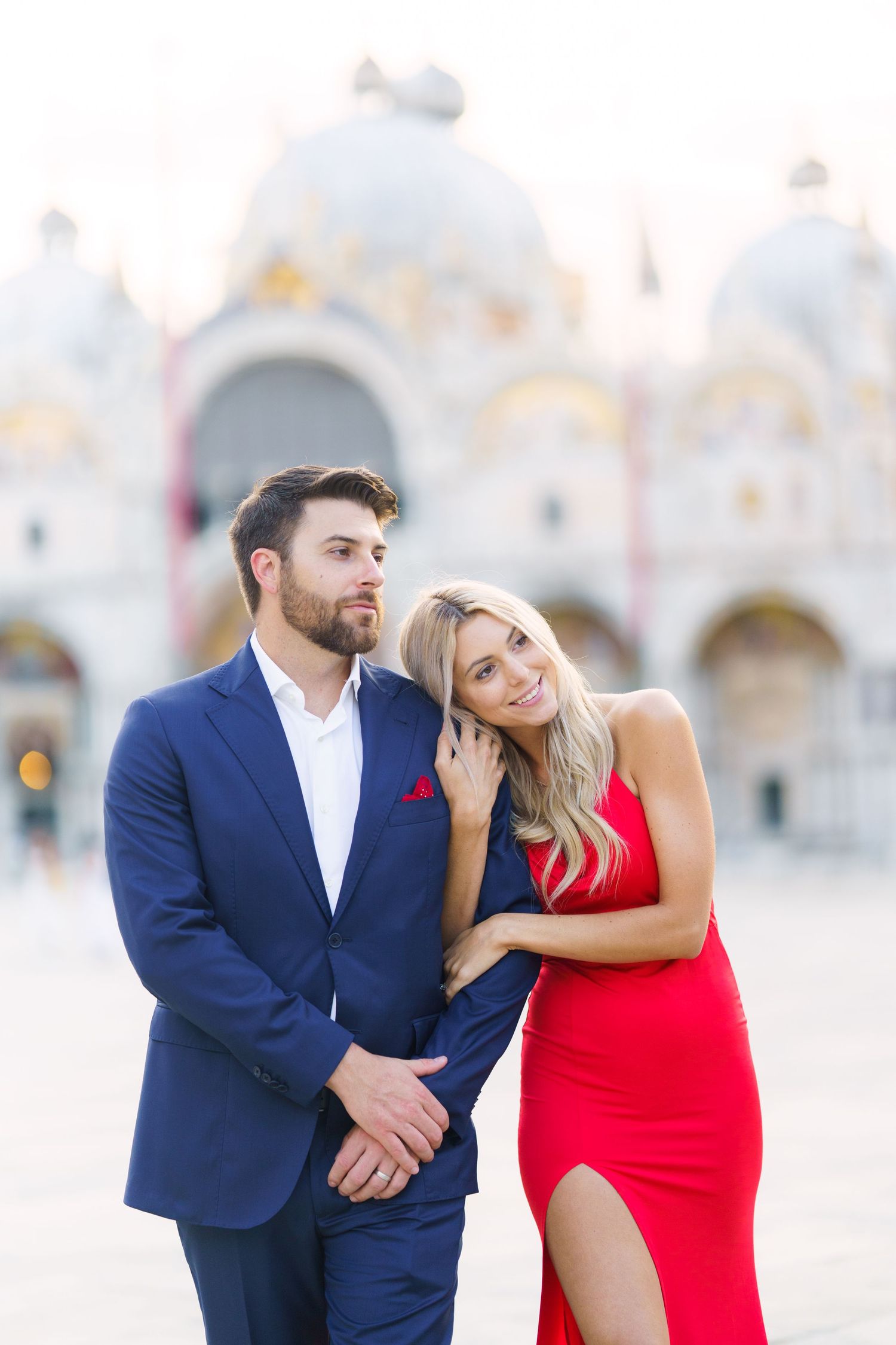 A couple in formal attire shares romantic moments on a beach at sunset.