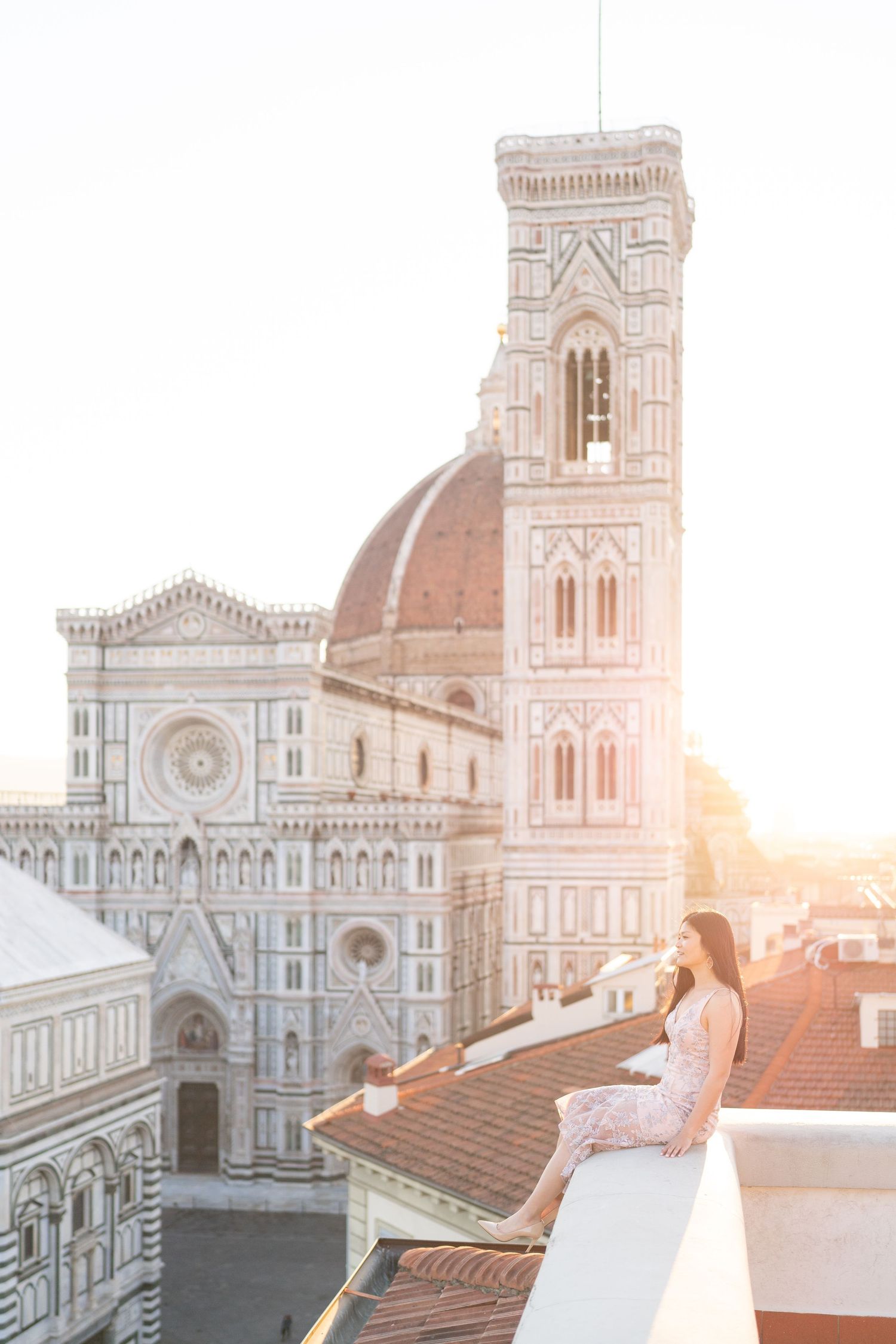 Woman in white dress overlooking Florence Cathedral and Giotto's Bell Tower during golden sunset in Italy.
