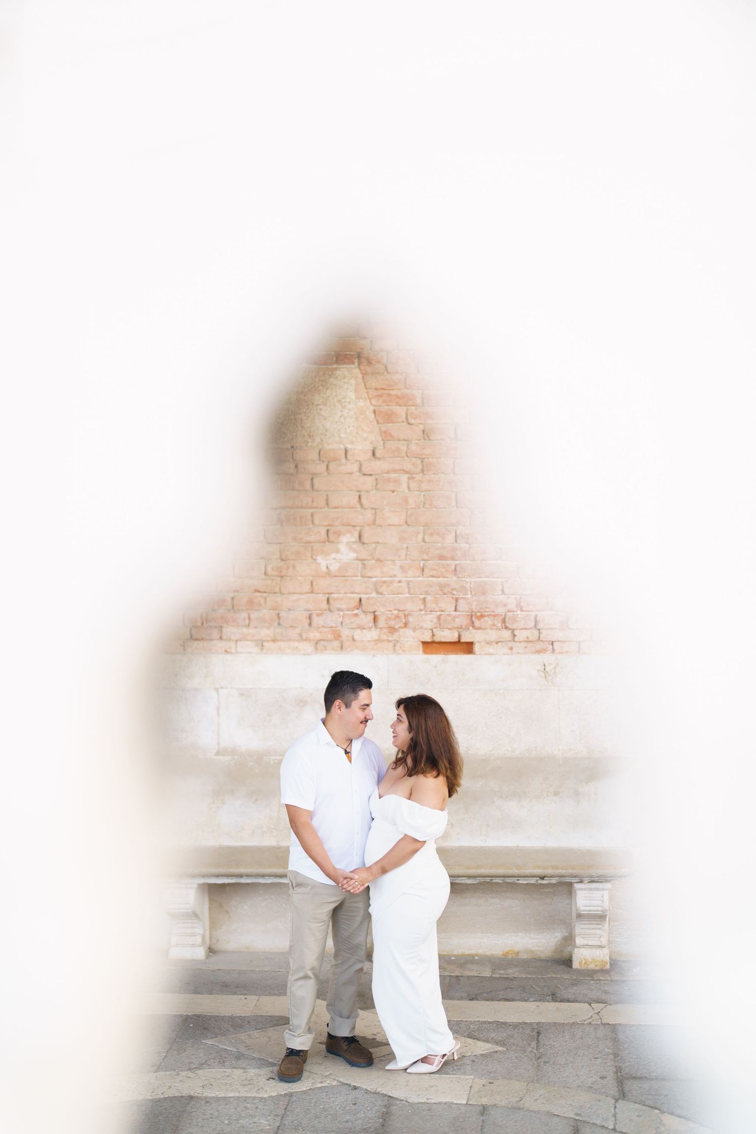 A couple in white outfits share romantic moments against a brick wall in a series of connected photos.