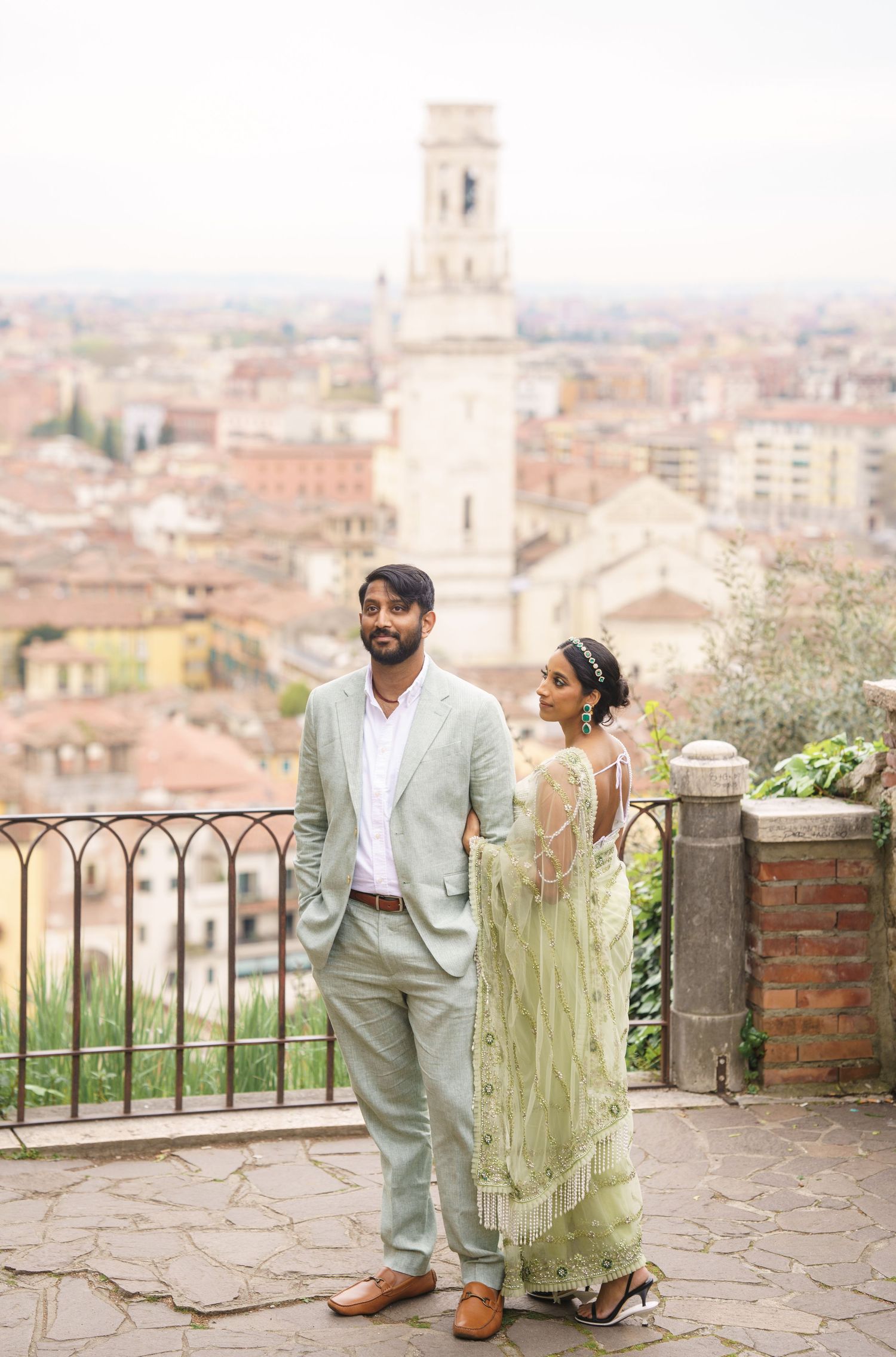 A couple in elegant attire poses together on a scenic terrace overlooking an Italian cityscape.