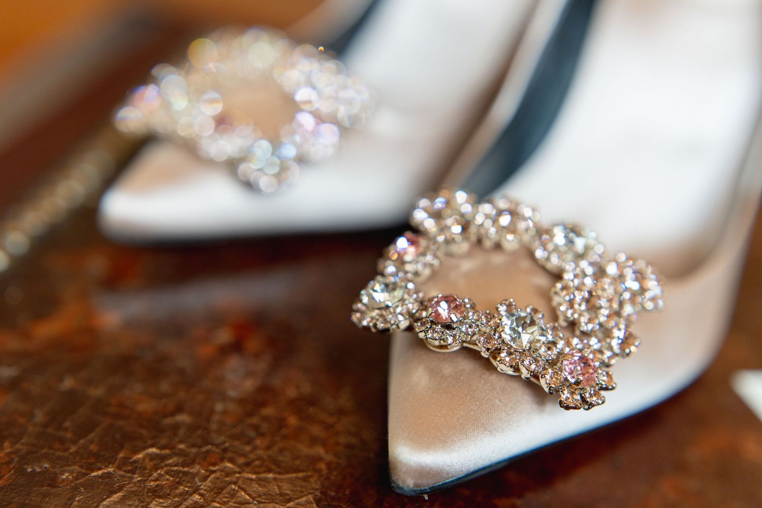 Crystal-embellished bridal shoes displayed on a rich wooden surface.