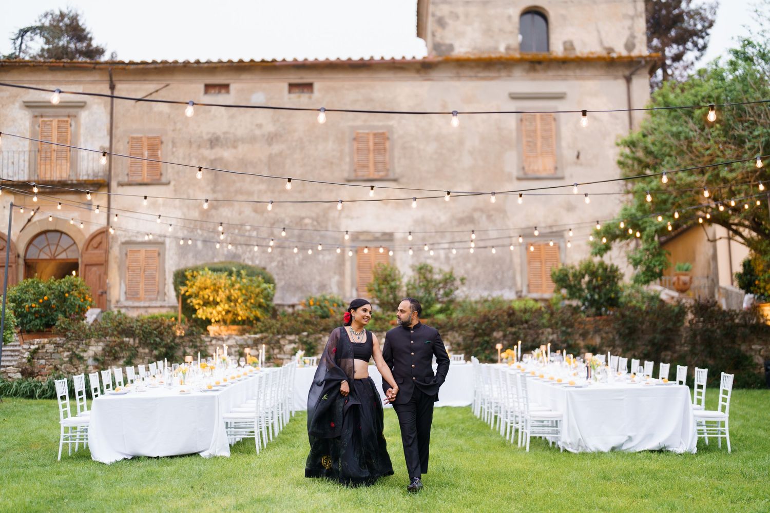 Outdoor wedding reception setup with white tables and string lights at a rustic villa venue.