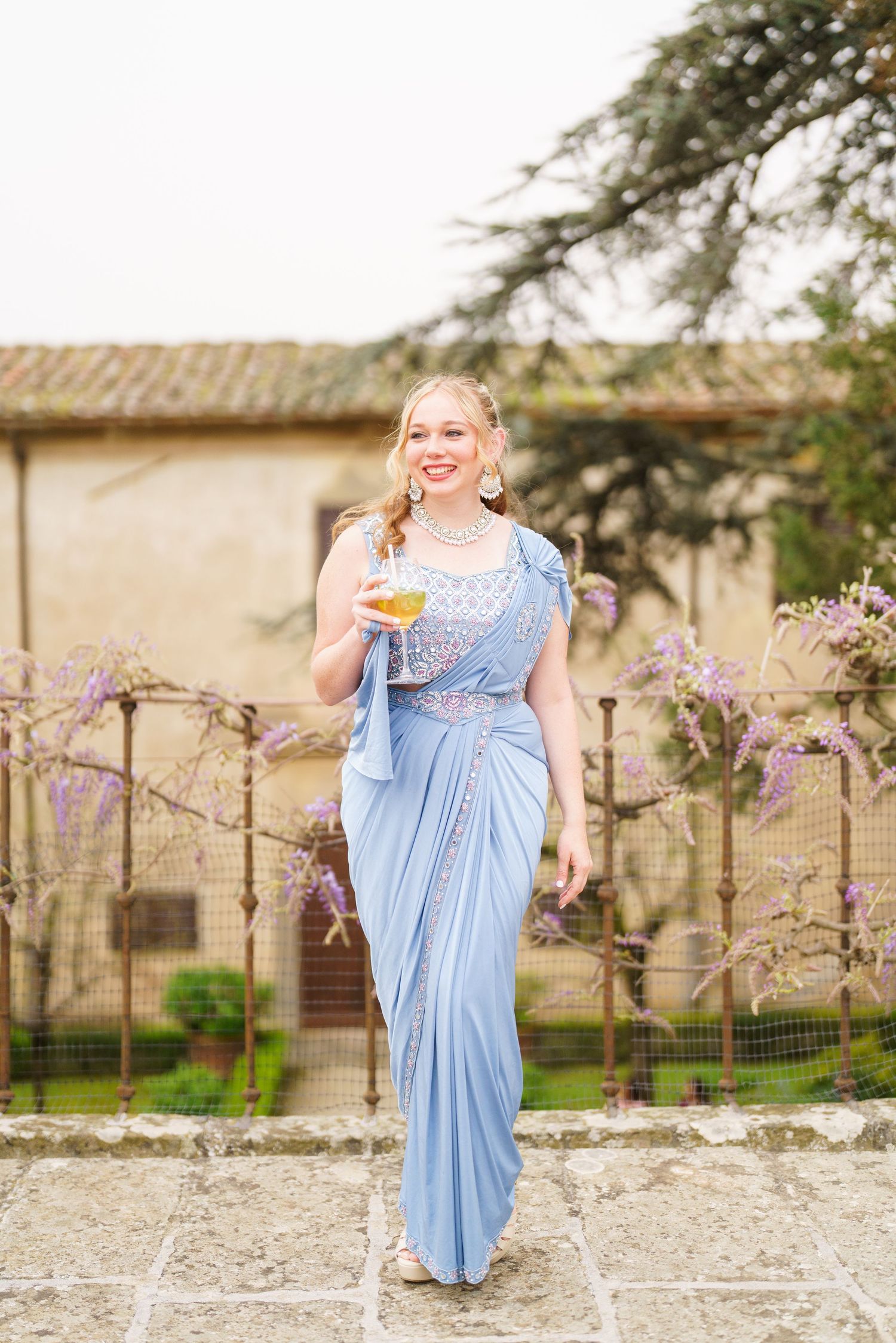 Person in flowing blue dress twirling joyfully in front of blooming spring trees.