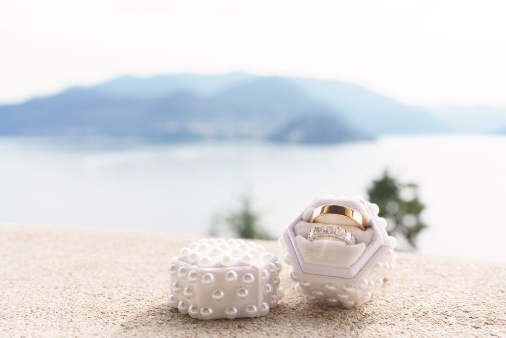 Wedding rings displayed on white sand with soft focus background.