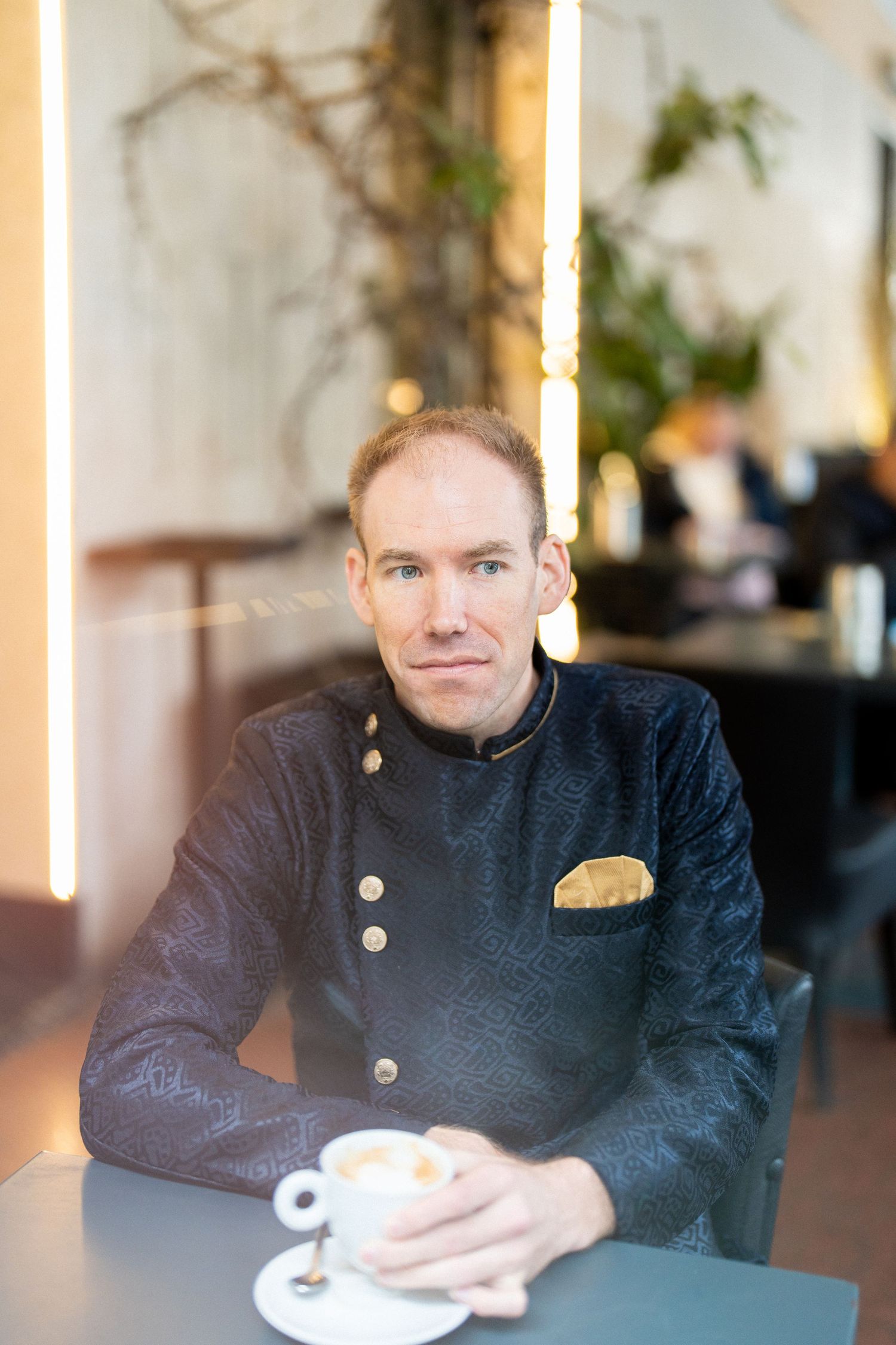 Person in formal black jacket seated at table in elegant indoor setting.