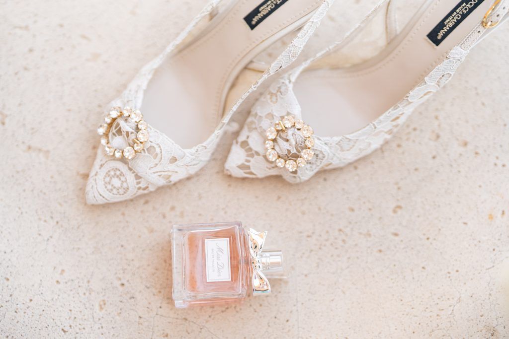 Wedding accessories including perfume bottles and delicate white shoes arranged on a light surface.