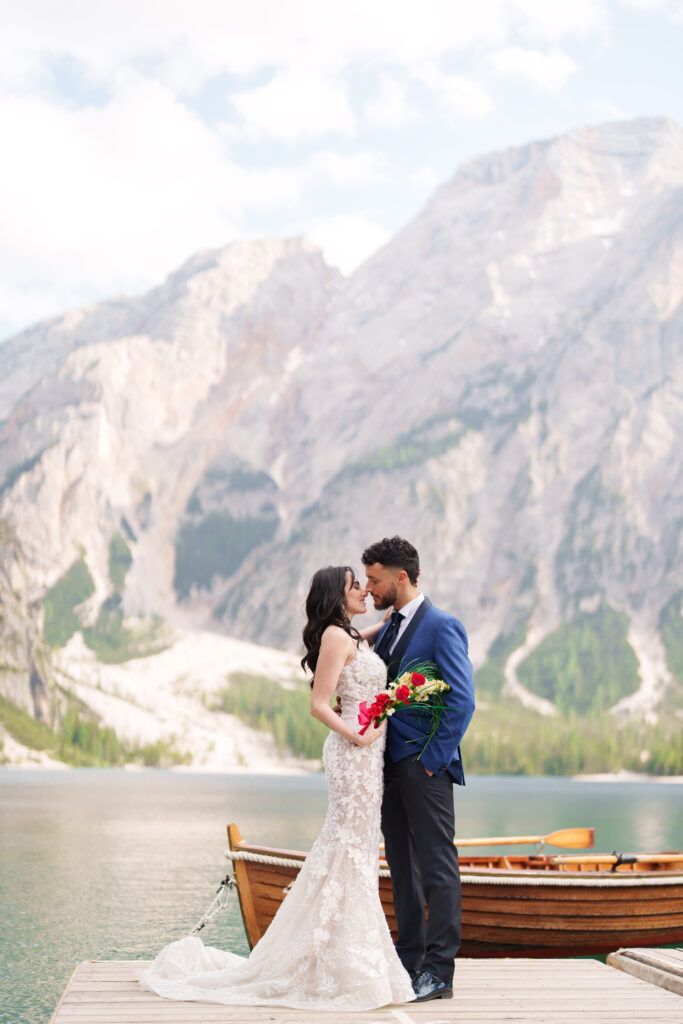 Romantic lakeside moment with dramatic mountain peaks and wooden boats in background.