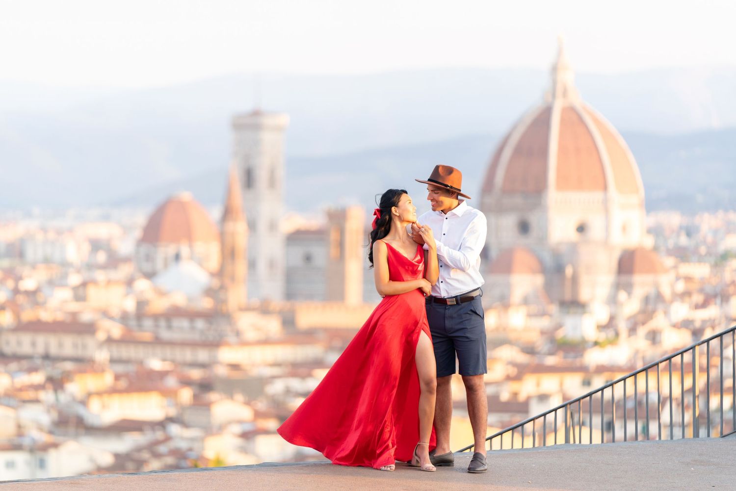 A couple stands at a scenic overlook in Florence, Italy with the iconic Duomo cathedral dome visible in the background.