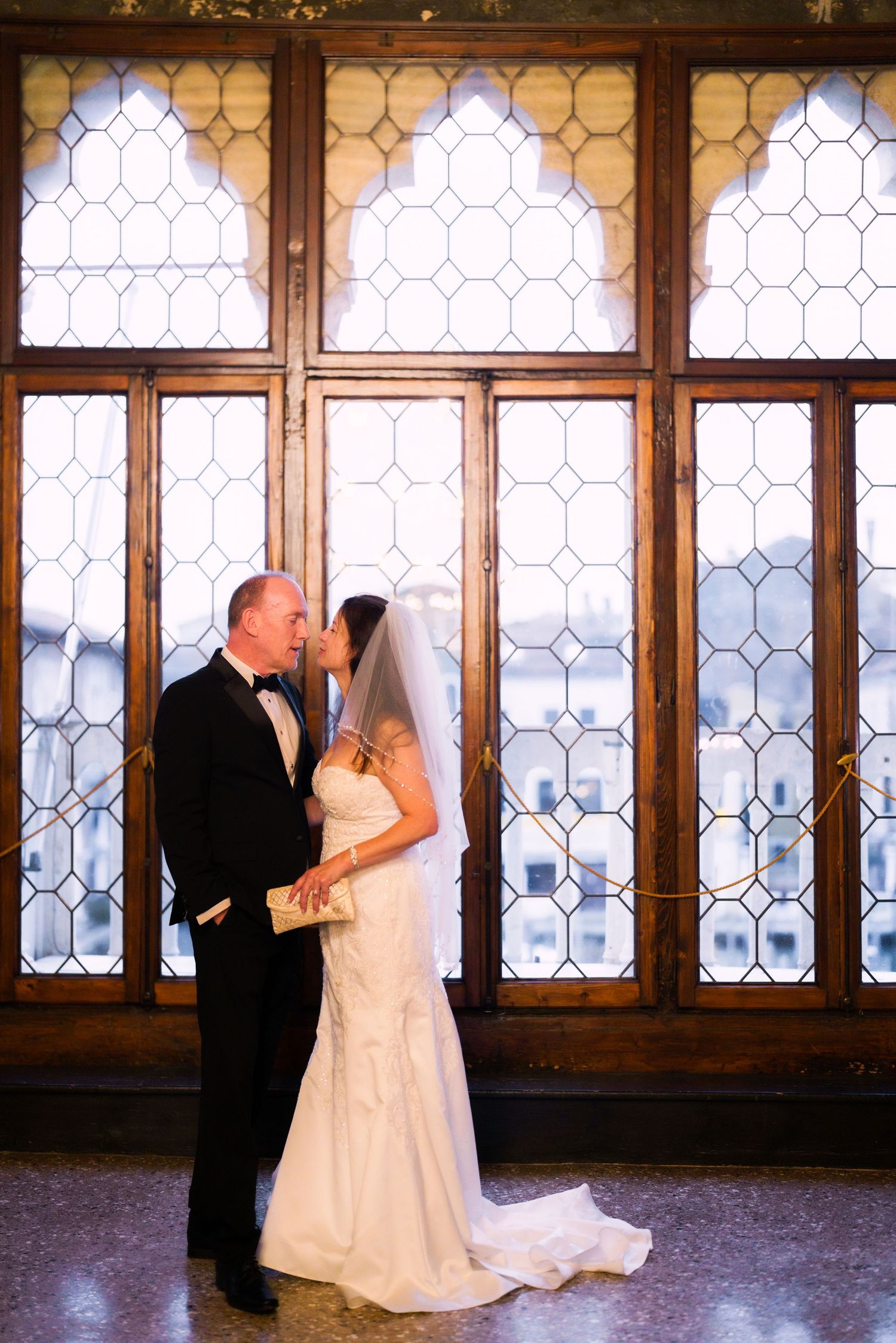 A romantic wedding photo series showing a couple dancing in front of ornate leaded glass windows in a historic venue.